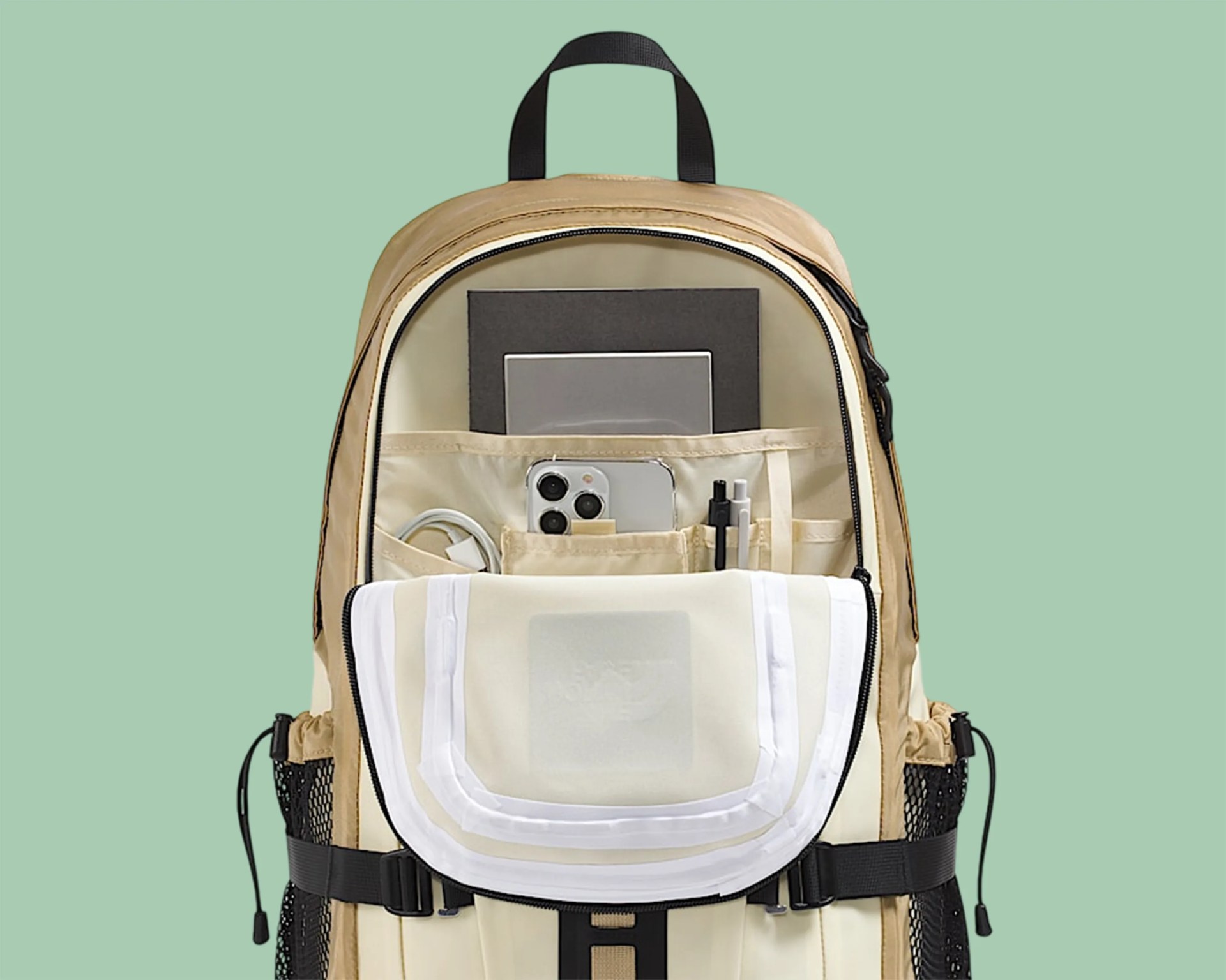 Beige and cream backpack with multiple compartments holding a smartphone, pens, cables, and notebooks.