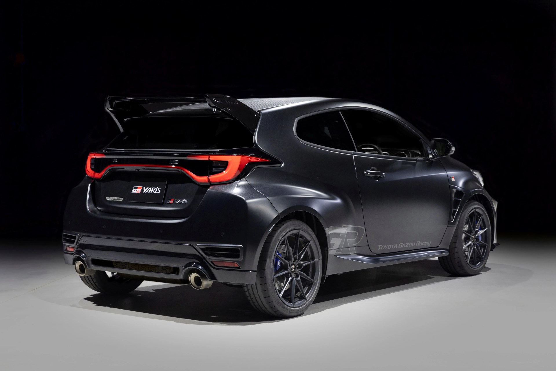 Matte black Toyota GR Yaris hatchback with rear spoiler and dual exhausts in a studio setting.