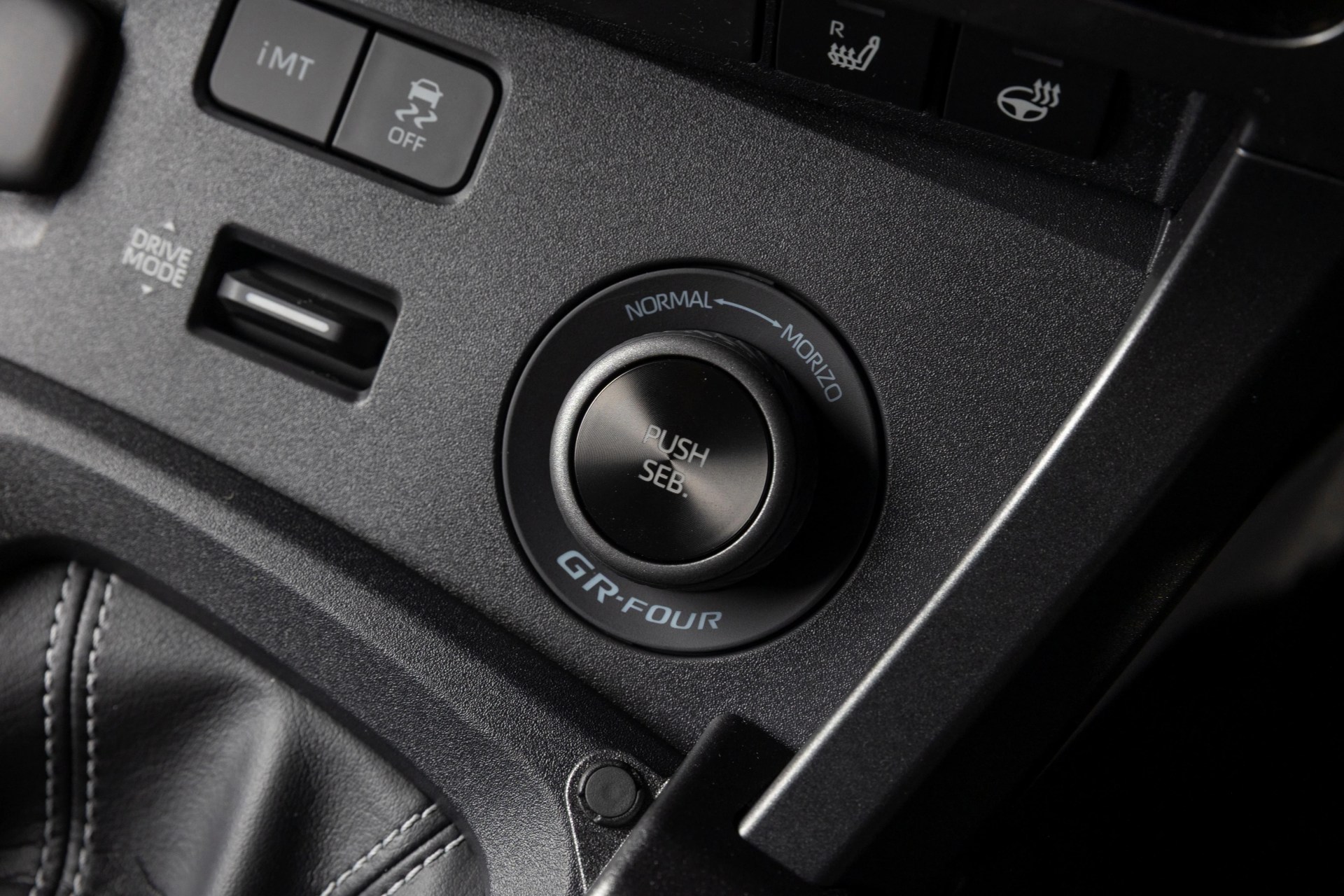 Black GR-FOUR drive mode selector knob with "PUSH SEB." text on a textured black car console.