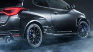 Matte black Toyota GR Yaris hatchback with blue brake calipers and "Toyota Gazoo Racing" decal on the side.