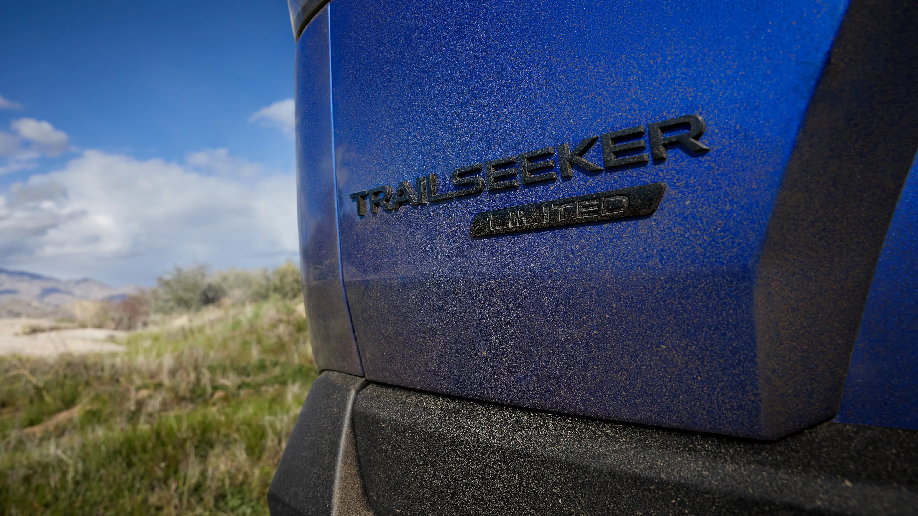 Close-up of a blue vehicle's rear with "TRAILSEEKER LIMITED" badge and dust on the surface.