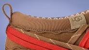 Close-up of a brown UGG shoe with red and beige fabric details and a loop at the heel.
