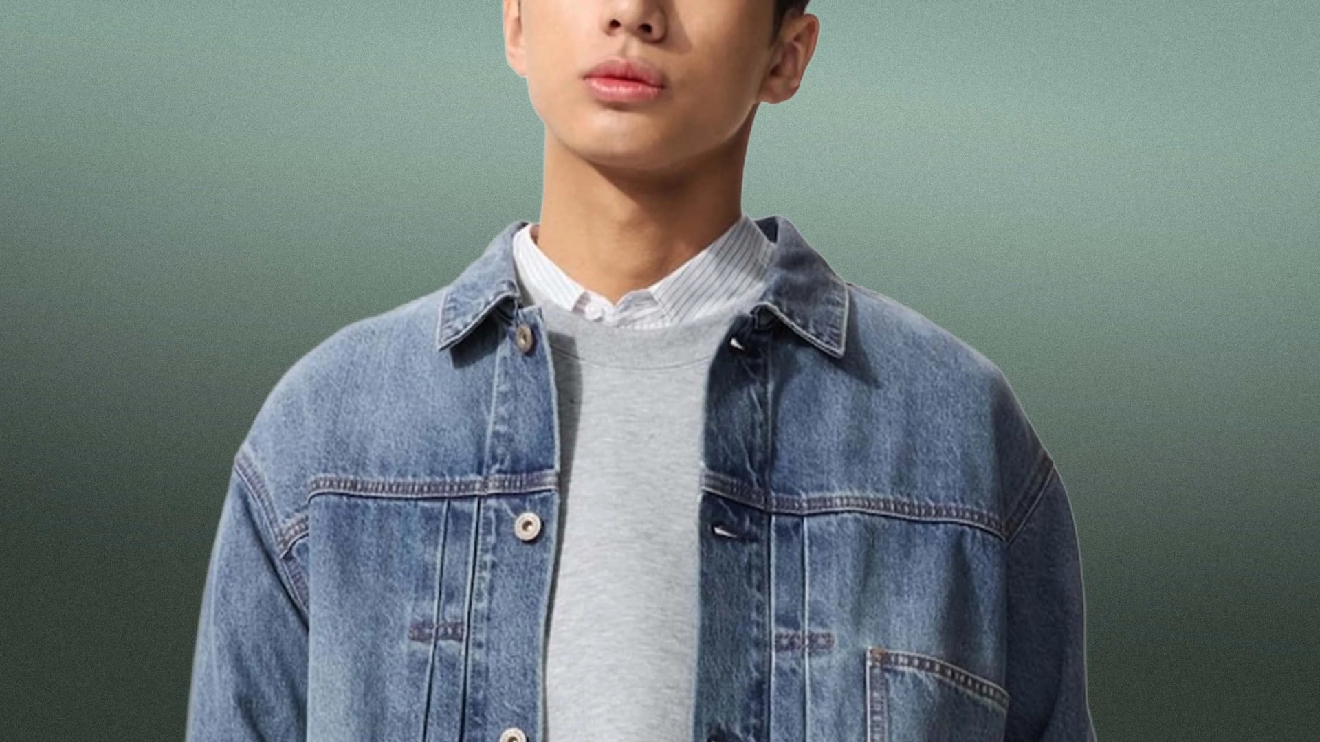 Person wearing a light blue denim jacket over a gray sweatshirt and a white collared shirt.