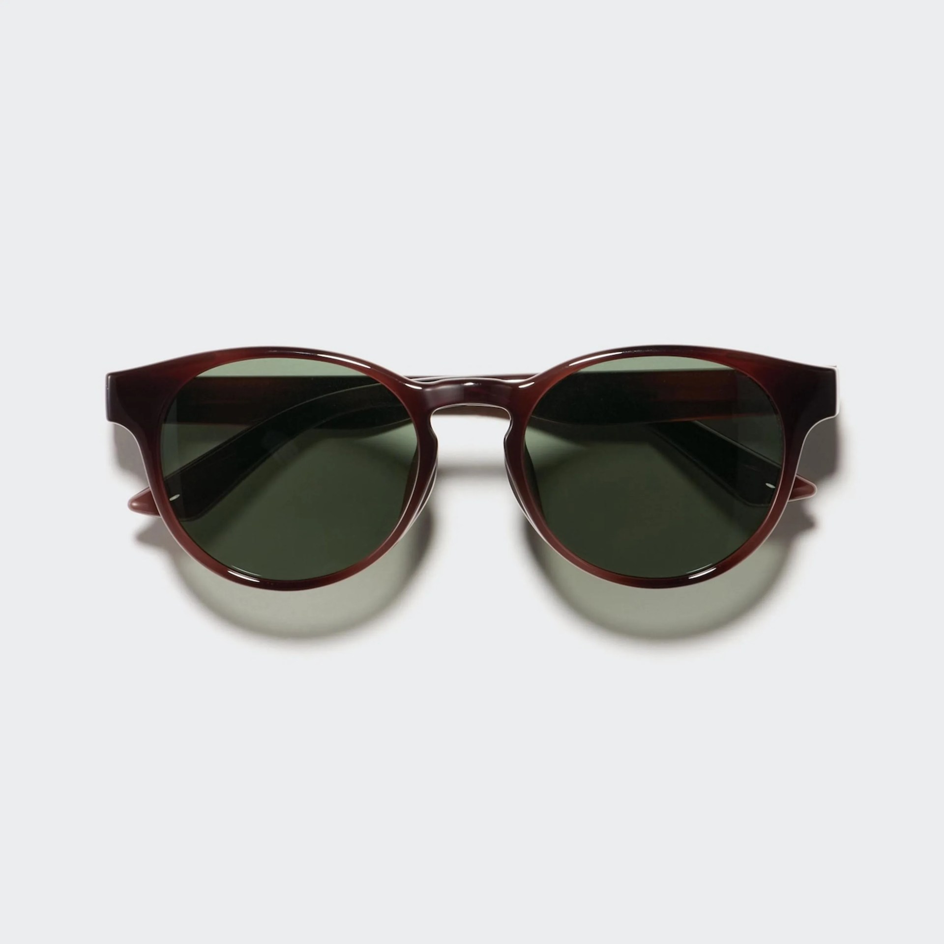 Round sunglasses with dark green lenses and glossy dark brown frames on a light gray background.