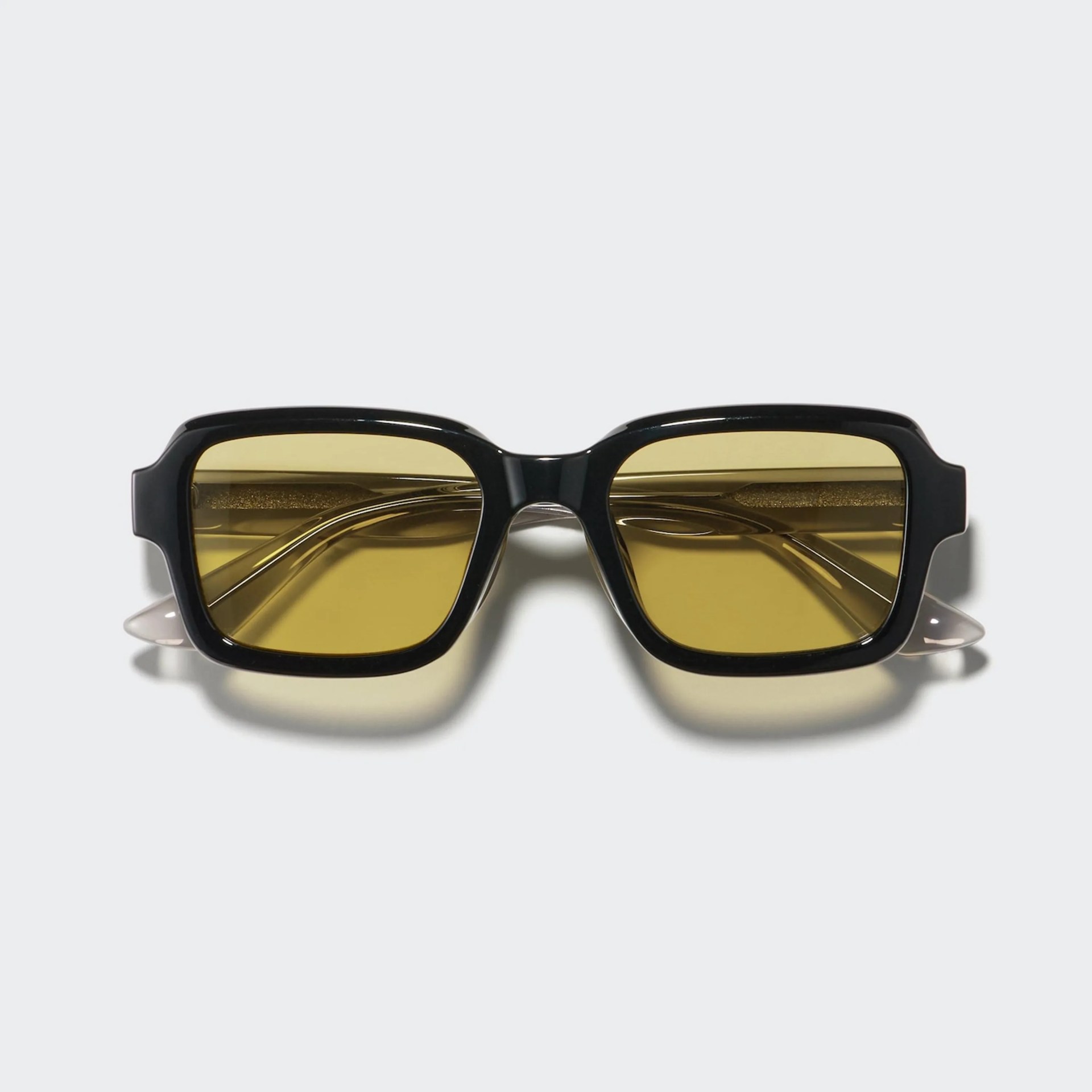 Black rectangular sunglasses with yellow tinted lenses and translucent beige temple tips.