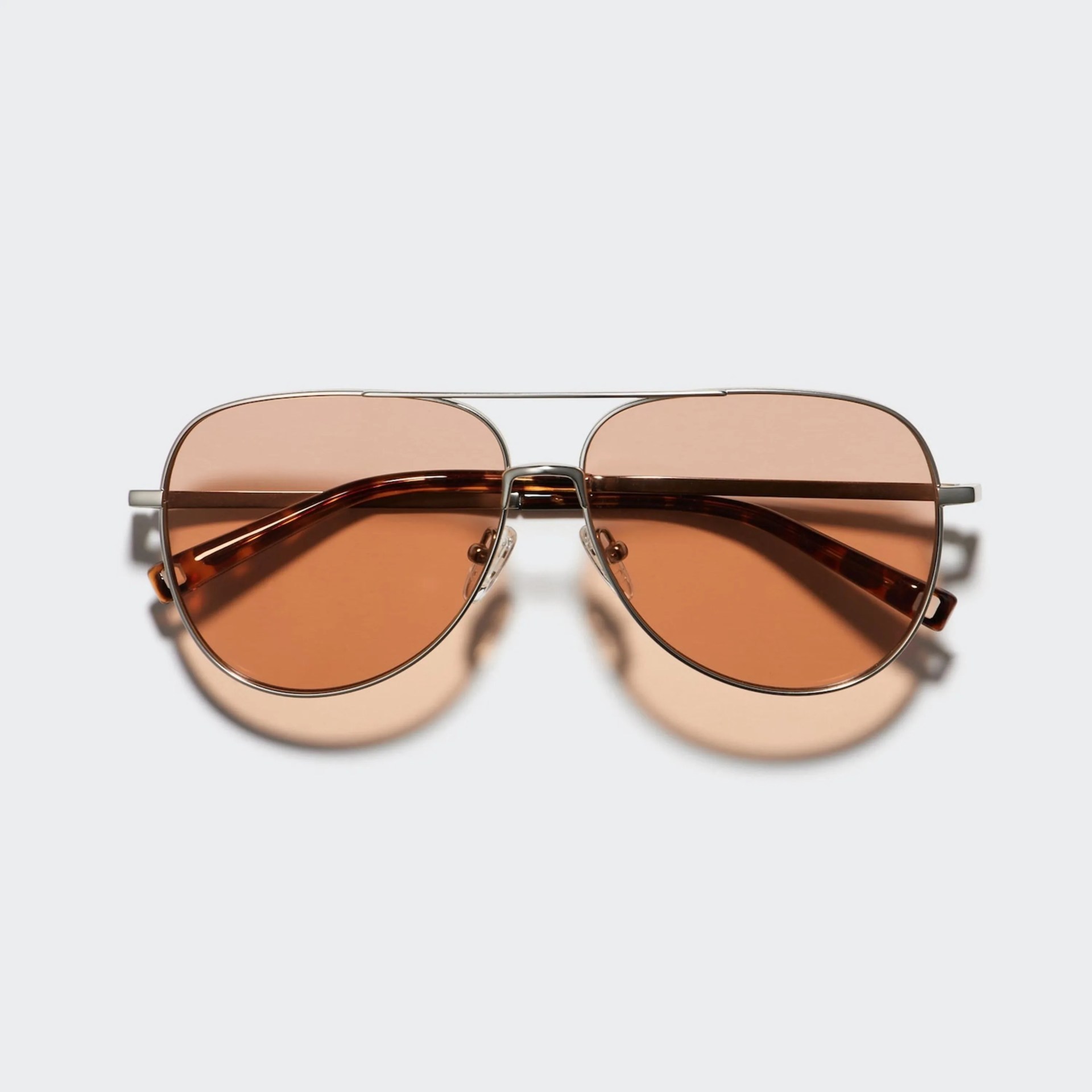 Aviator-style sunglasses with thin silver metal frames and brown tinted lenses on a light background.