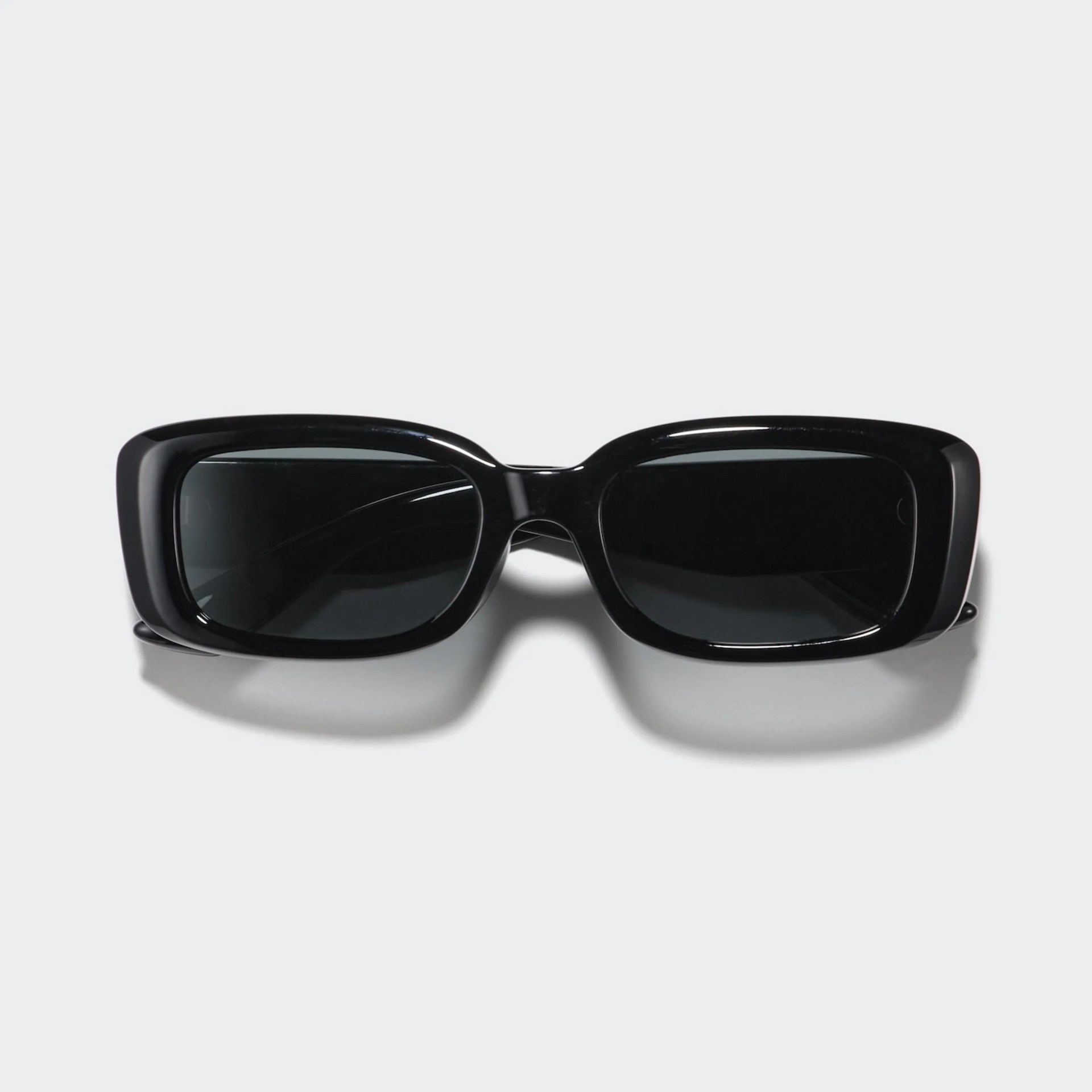 Black rectangular sunglasses with thick glossy frames and dark lenses on a light gray background.