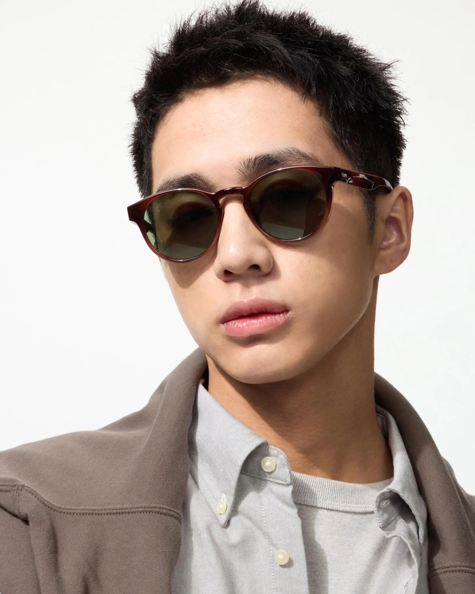 Brown round sunglasses with dark lenses worn by a person in a gray shirt and brown jacket.