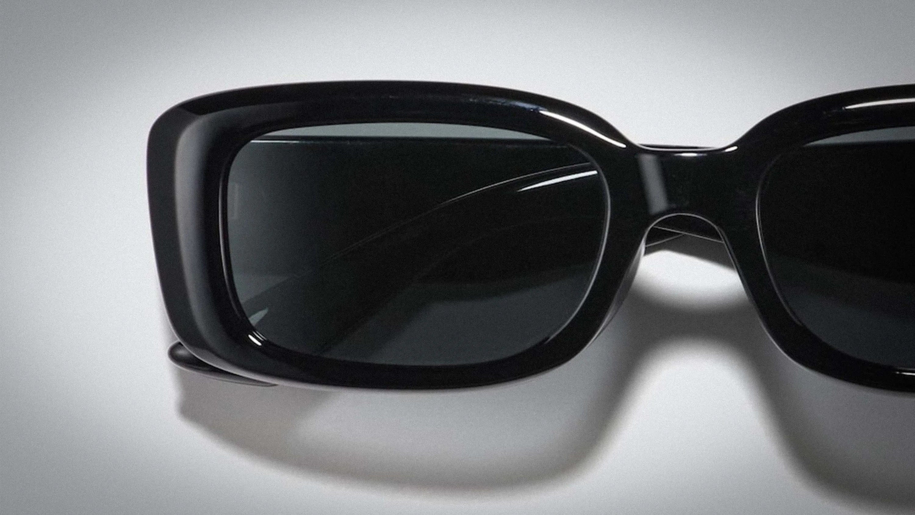 Close-up of black rectangular sunglasses with thick glossy frames on a white surface.
