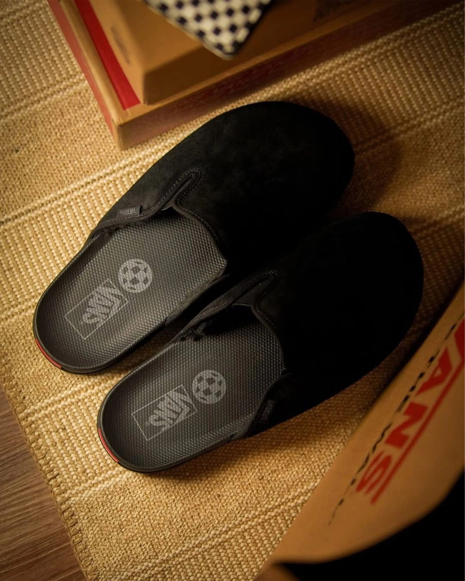 Pair of black Vans slip-on slippers with textured insoles on a woven beige rug.