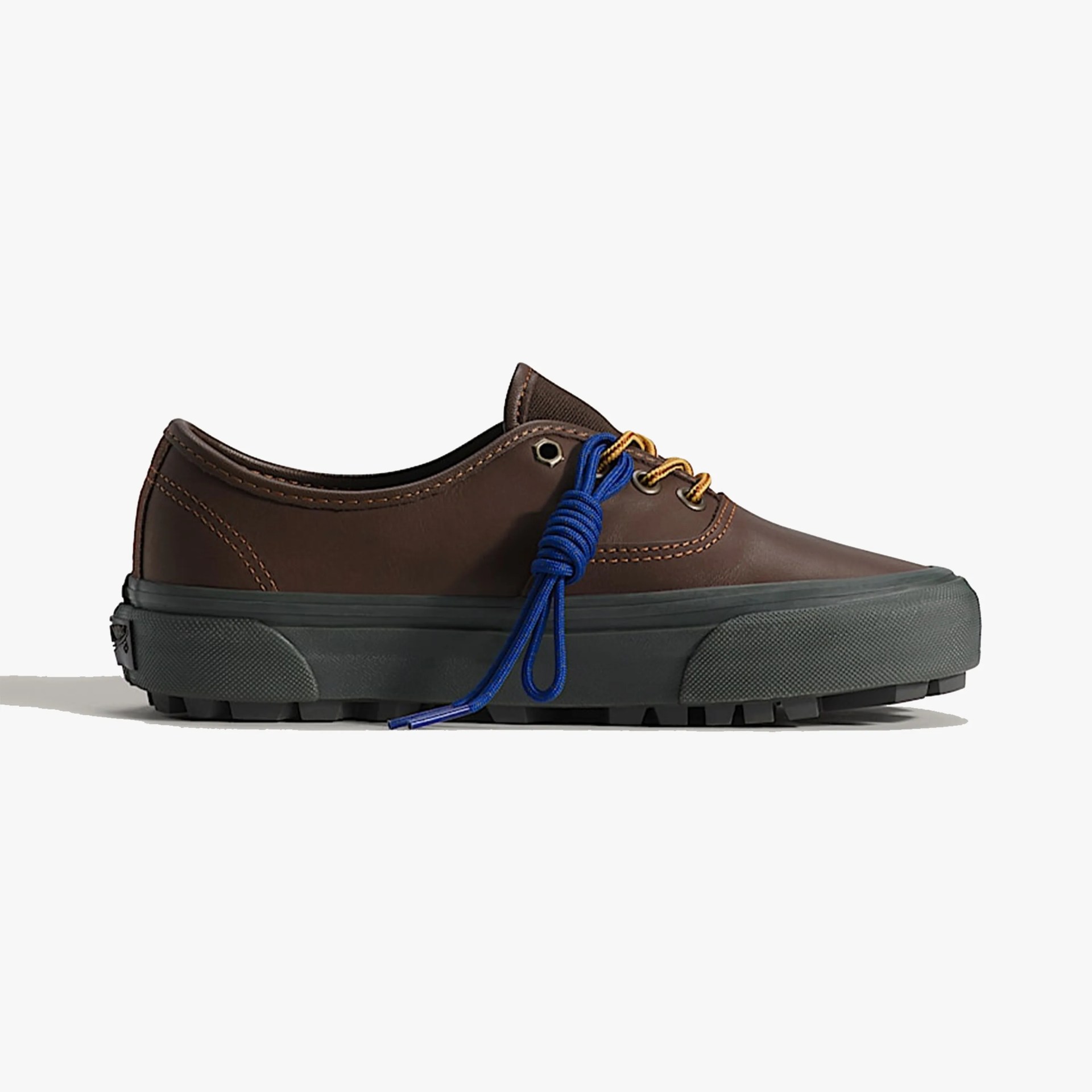 Low-top brown leather sneaker with black thick rubber sole and blue and yellow laces tied in a knot.