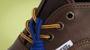 Close-up of brown leather boot with yellow and brown laces threaded through metal eyelets and a blue lace tied in a knot.
