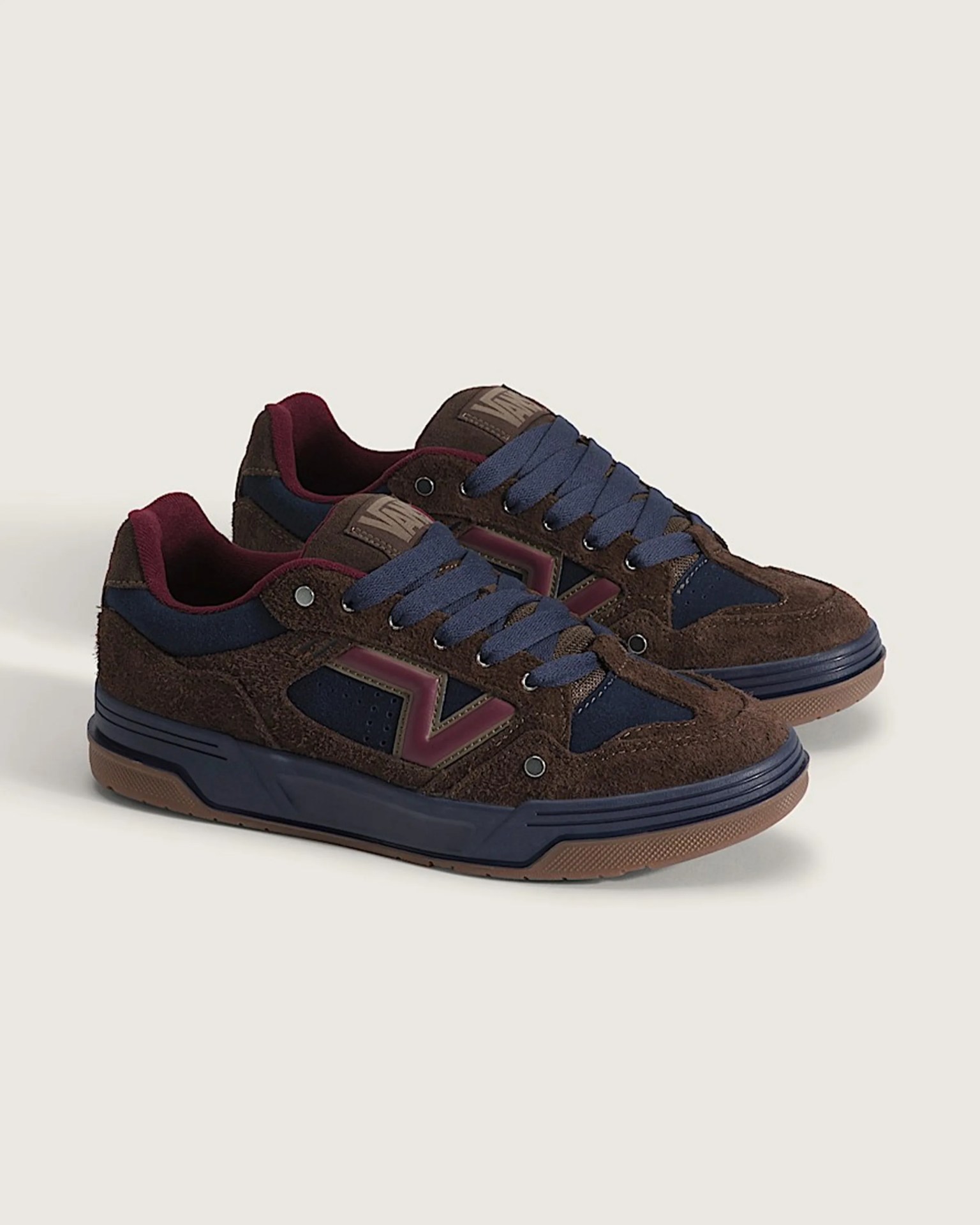Pair of brown suede sneakers with navy blue accents, burgundy lining, and blue laces on a light background.