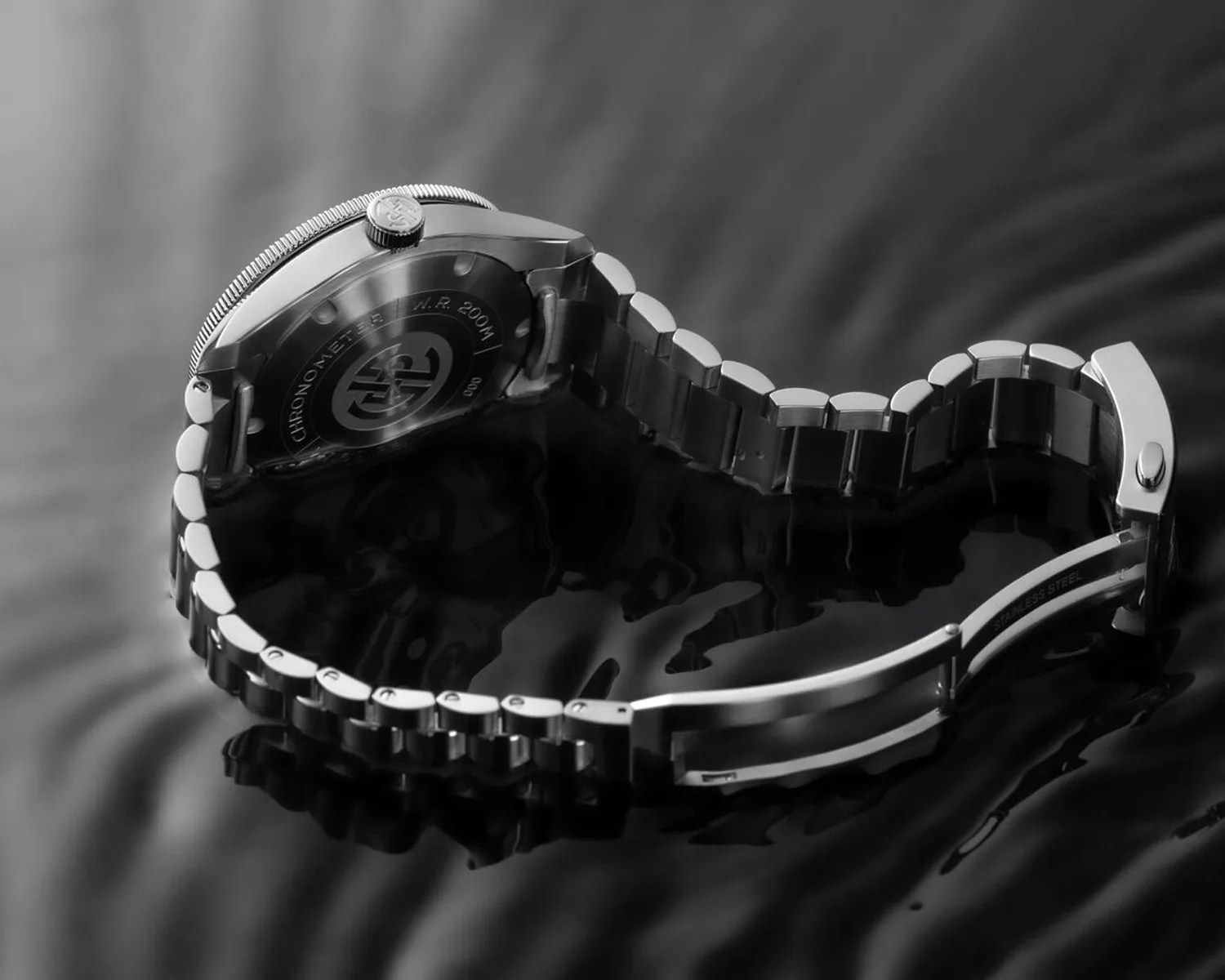 Stainless steel wristwatch with metal link bracelet and engraved case back on a reflective black surface.
