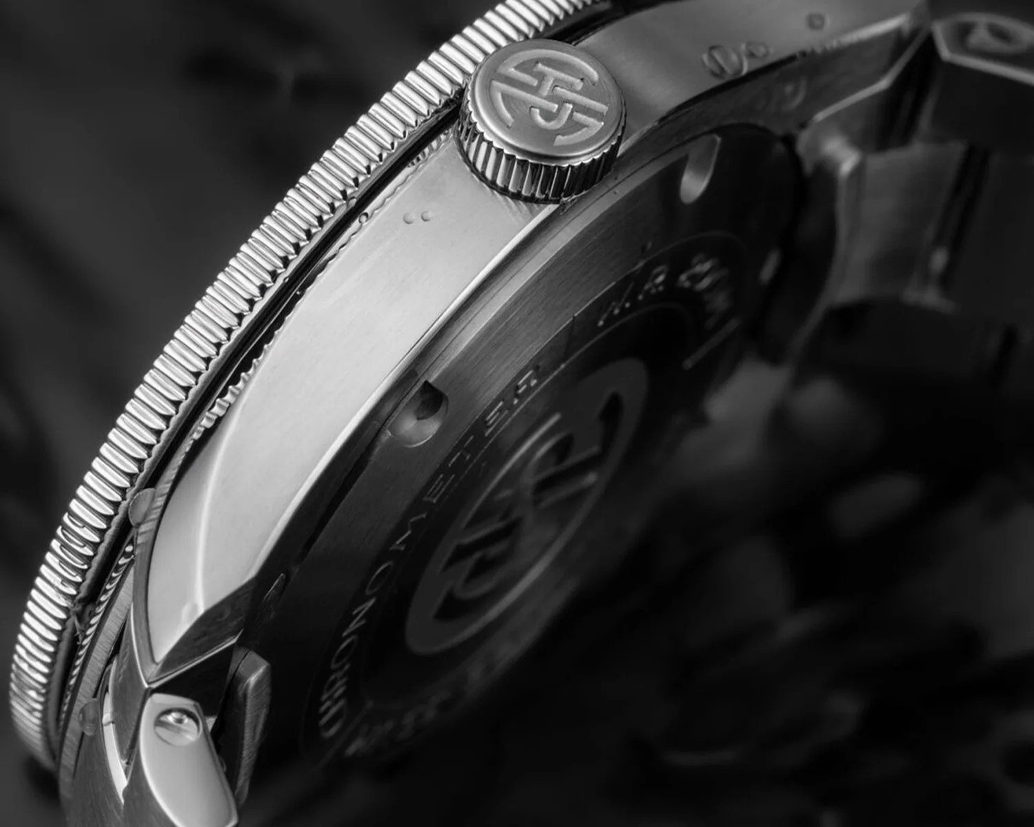 Close-up of a stainless steel watch case back and crown with engraved logo and knurled bezel.