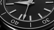 Close-up of a black watch face with silver hour markers and hands, showing the 30 and 40-minute marks on the bezel.