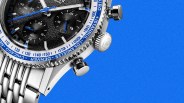 Close-up of a silver chronograph watch with a black textured dial, blue accents, and a stainless steel bracelet on a blue background.