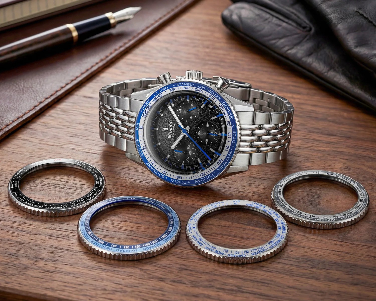 Silver chronograph wristwatch with black dial and blue accents, surrounded by four interchangeable bezels on a wooden surface.