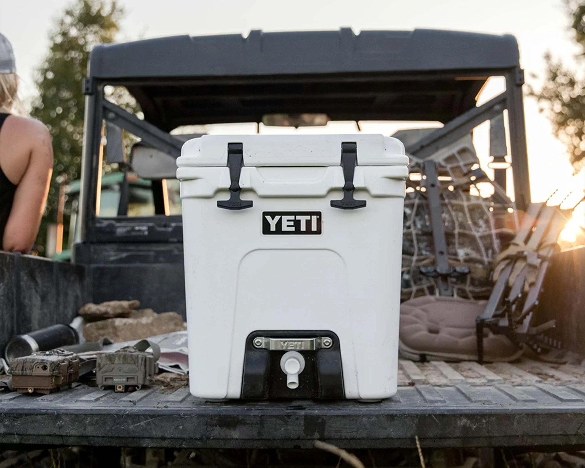 White YETI cooler with black latches and a spout on the back of a pickup truck bed.