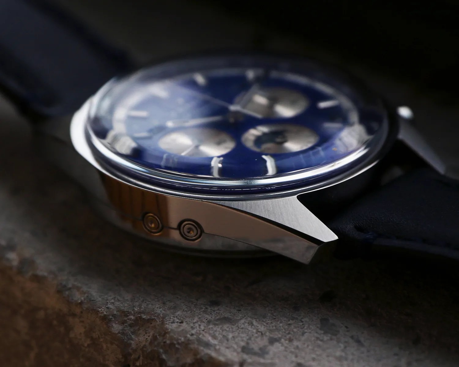 Close-up of a silver watch case with a blue dial and blue leather strap resting on a textured surface.