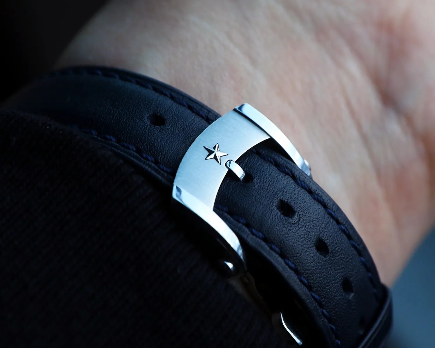Close-up of a blue leather watch strap with blue stitching and a silver buckle featuring a star emblem.