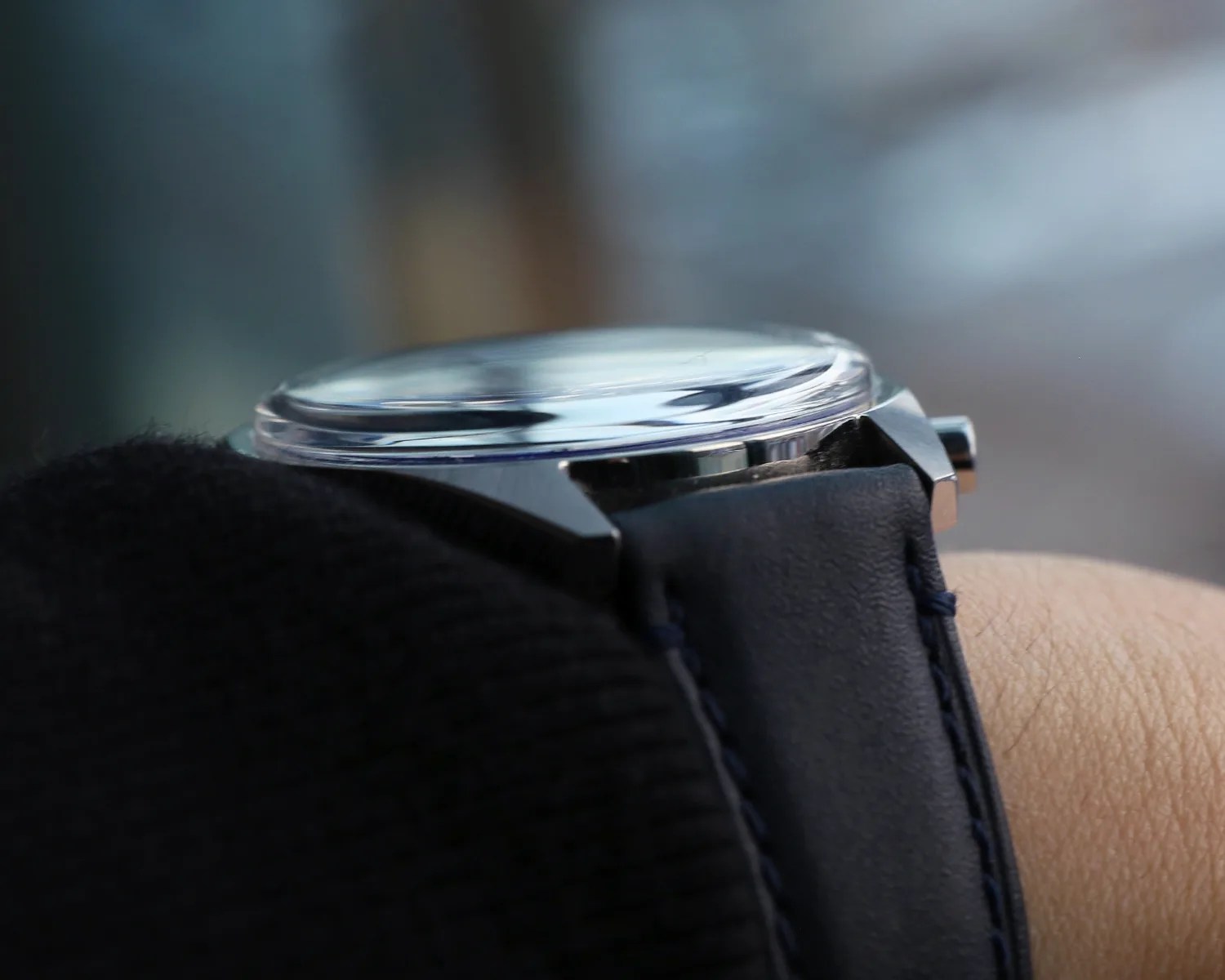 Close-up of a wristwatch with a domed crystal and blue leather strap worn on a wrist.
