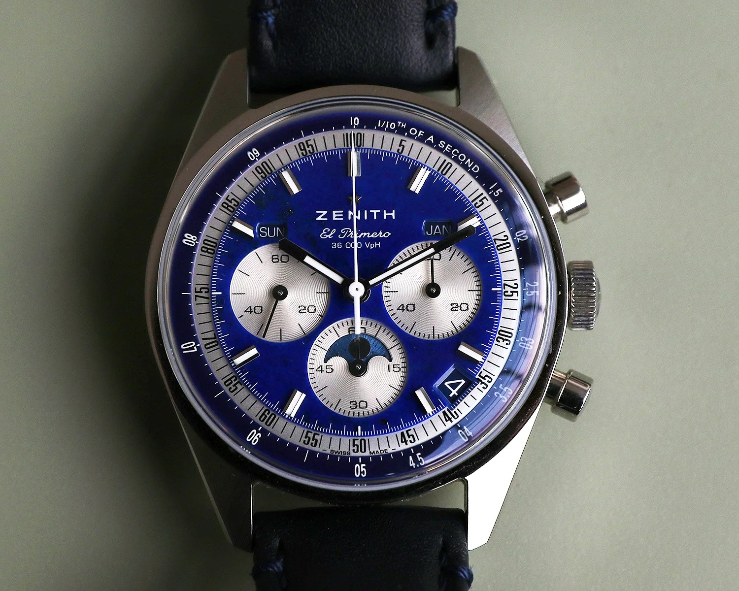 Round Zenith El Primero wristwatch with blue dial, three silver subdials, day and month windows, and black leather strap.