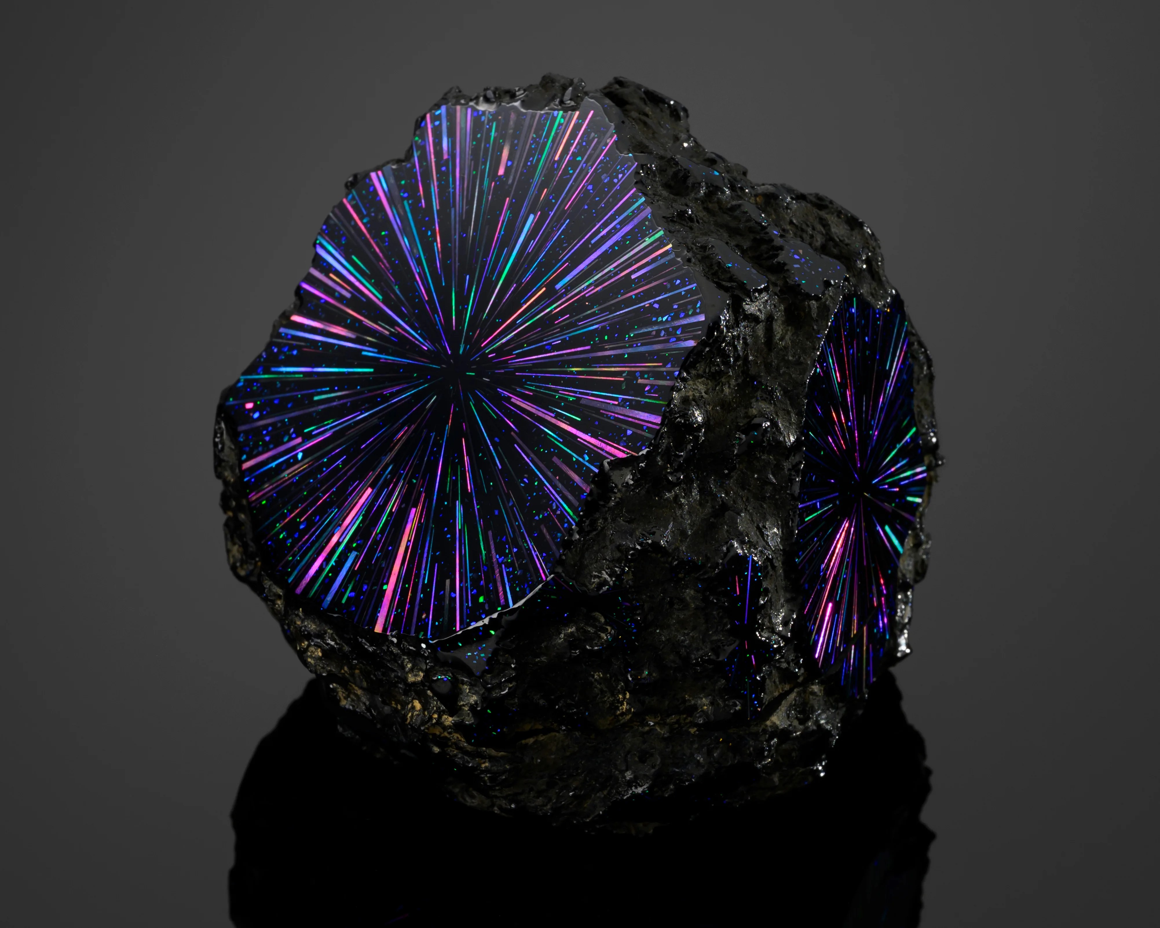 Black geode rock with iridescent, starburst-like purple, blue, and green patterns on its cut surfaces against a dark background.