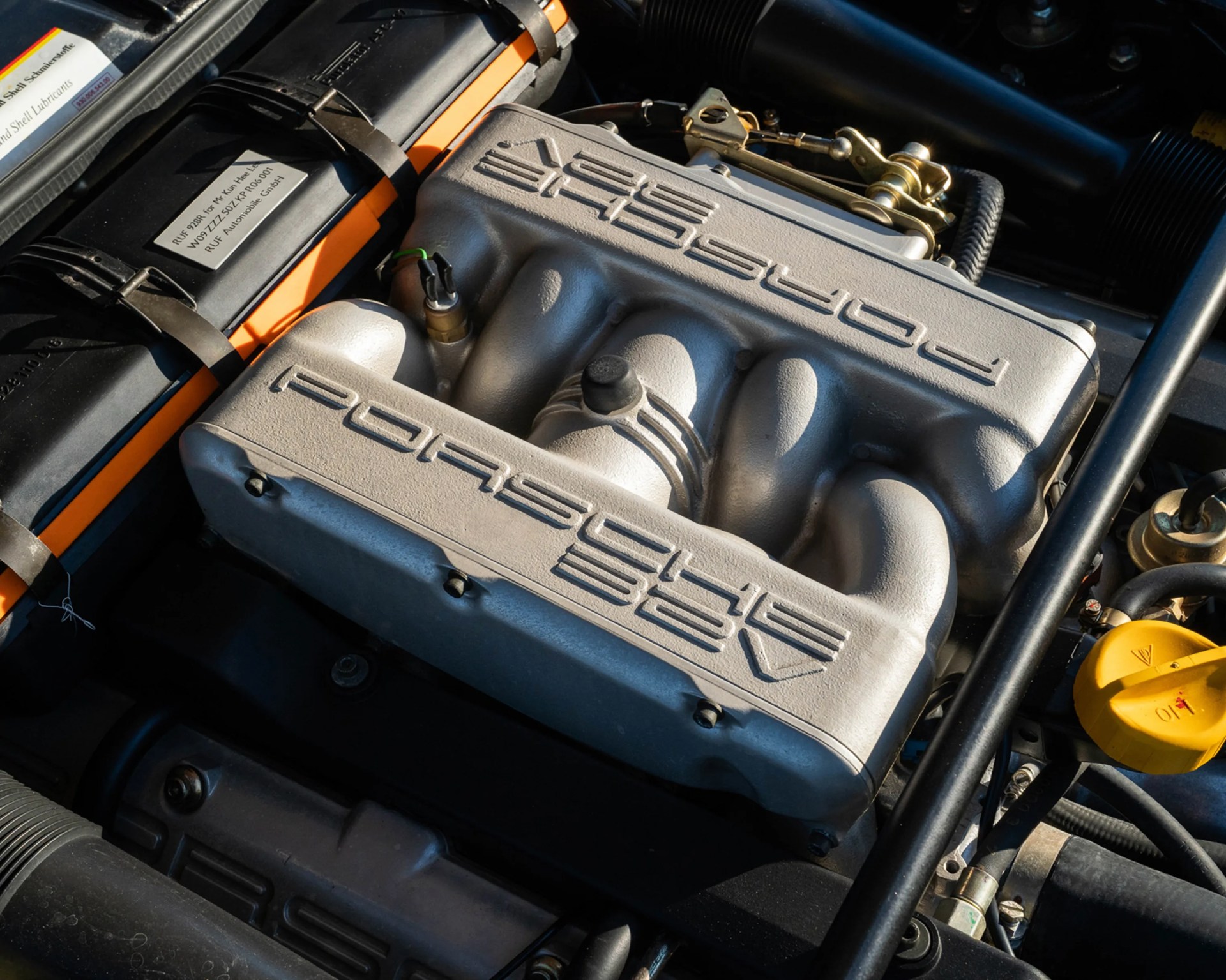 Silver Porsche 32V engine cover with embossed Porsche logo and intake manifold in an engine bay.