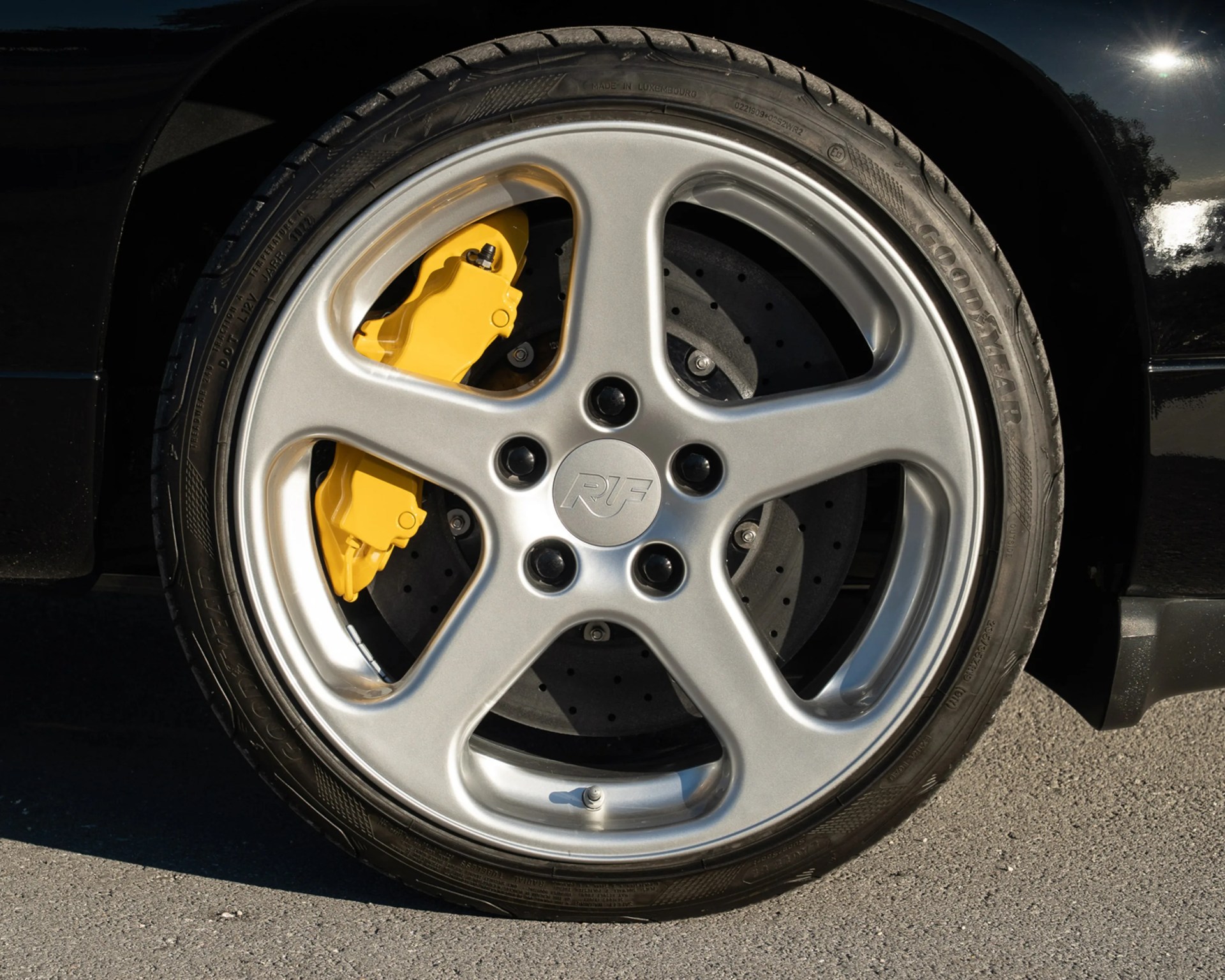 Silver five-spoke RUF alloy wheel with yellow brake caliper and Goodyear tire on a black car.