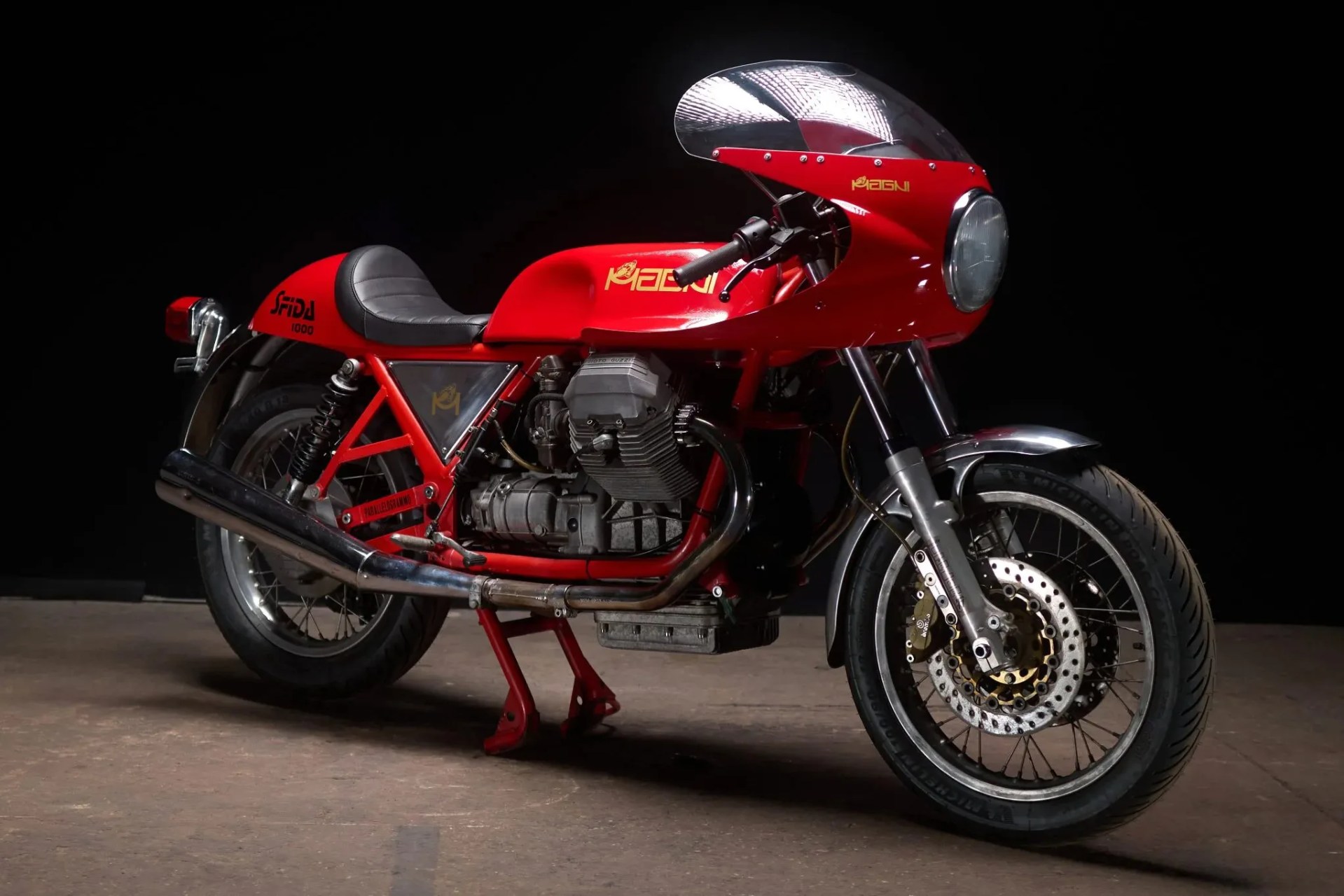 Red vintage Moto Guzzi motorcycle with black seat and chrome exhaust on a dark background.