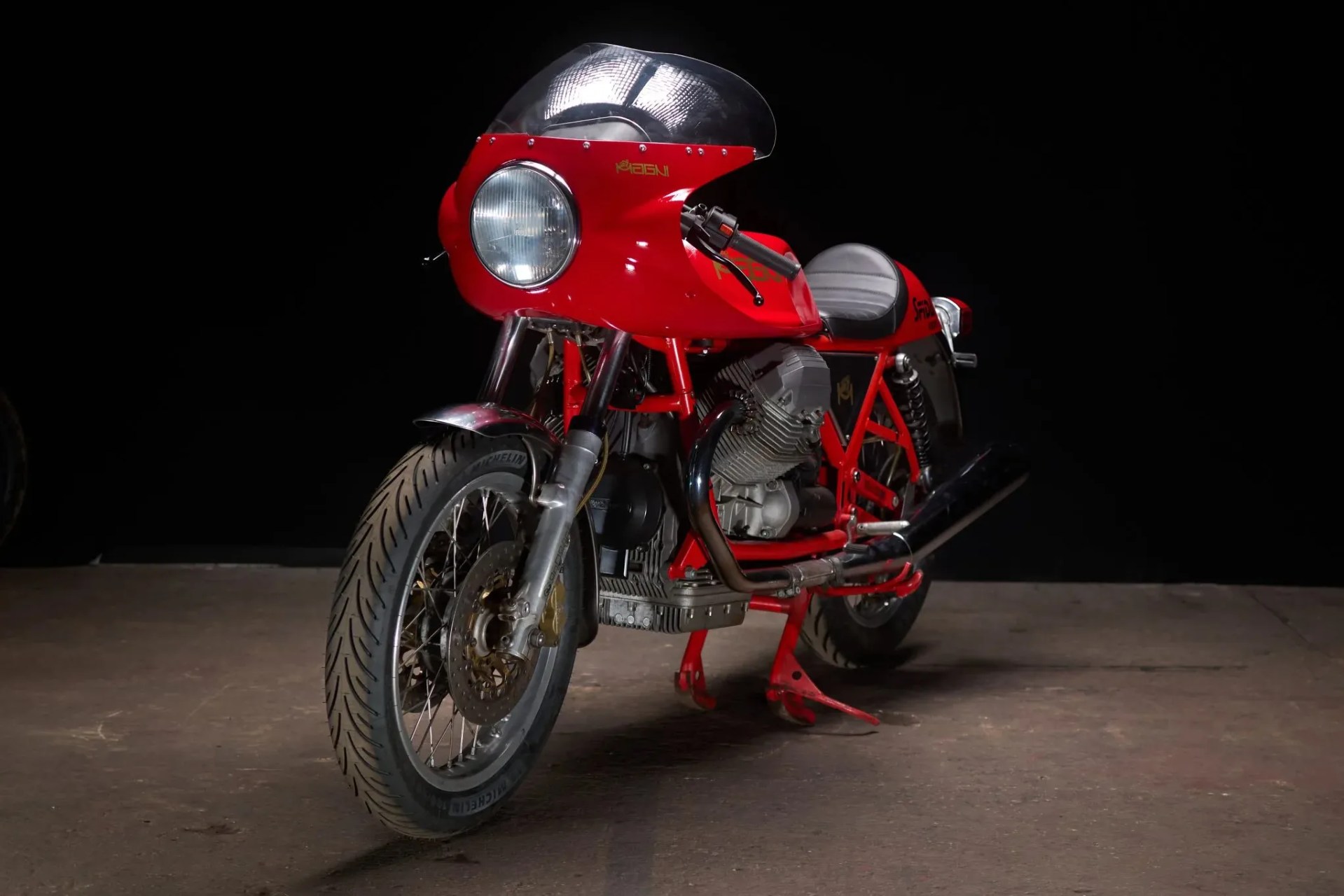 Red vintage racing motorcycle with a large front fairing and black exhaust pipes on a concrete floor.
