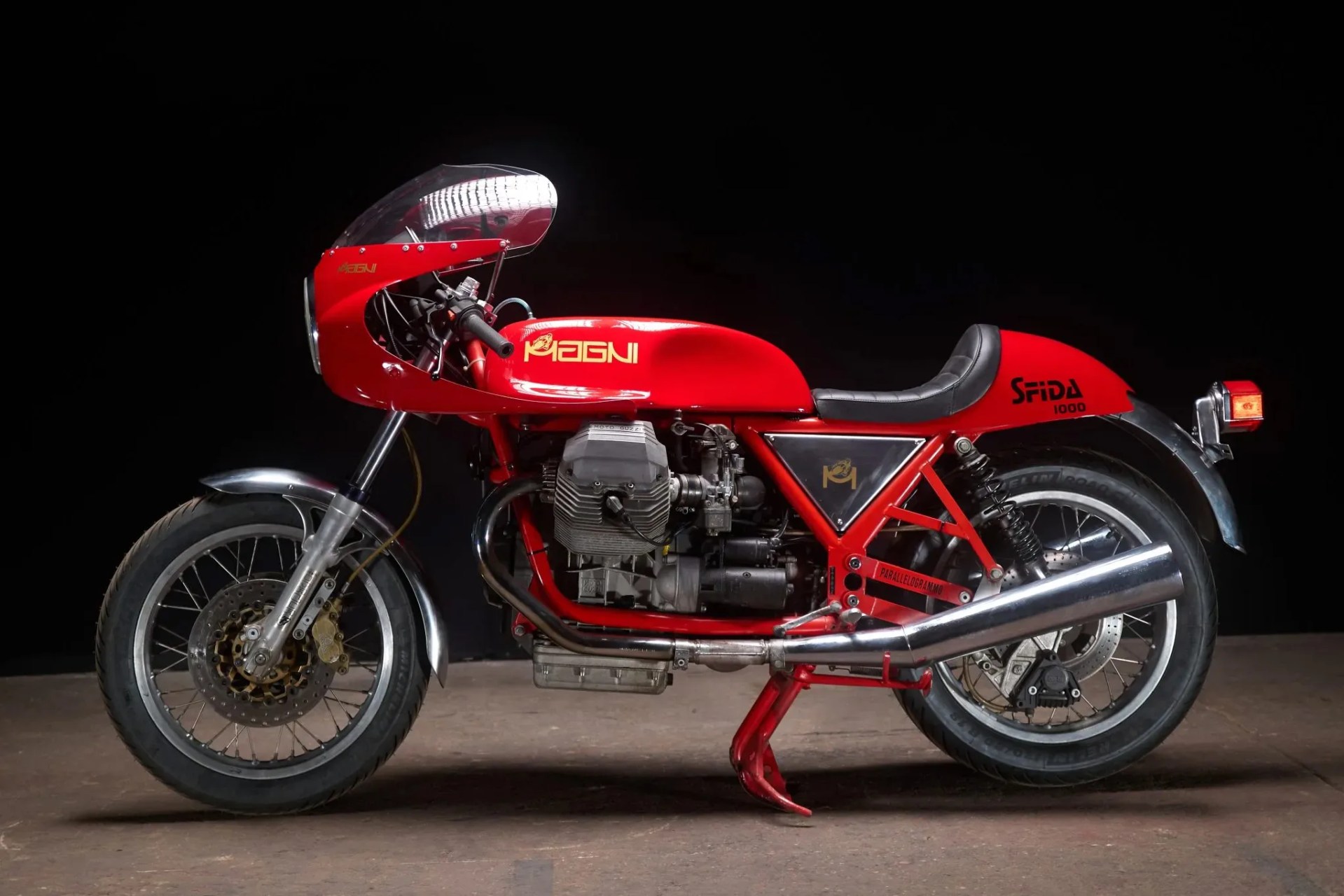 Red Magni Sfida 1000 motorcycle with black seat and chrome exhaust on a dark background.