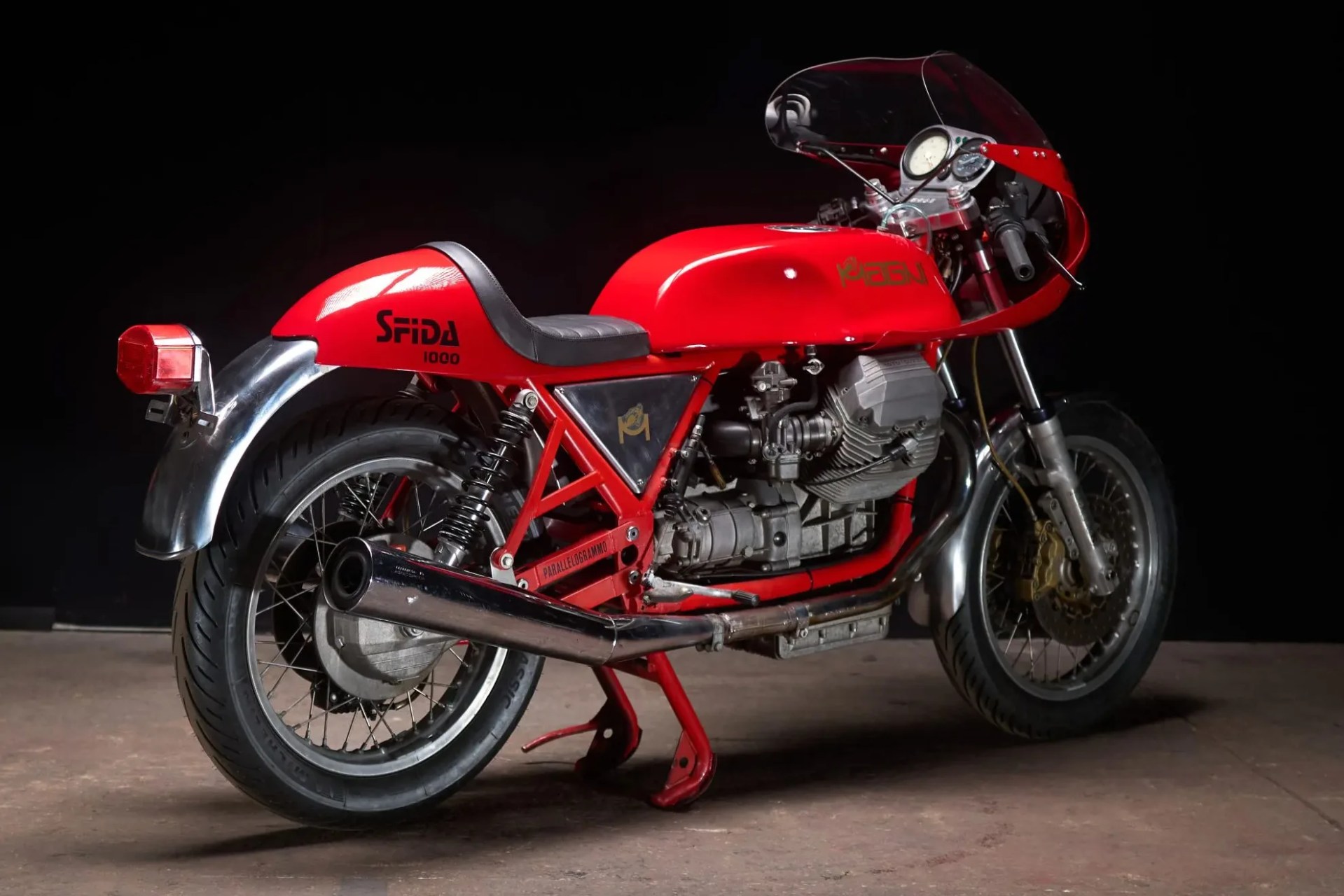 Red vintage Moto Guzzi Sfida 1000 motorcycle with black seat and chrome exhaust on a concrete floor.