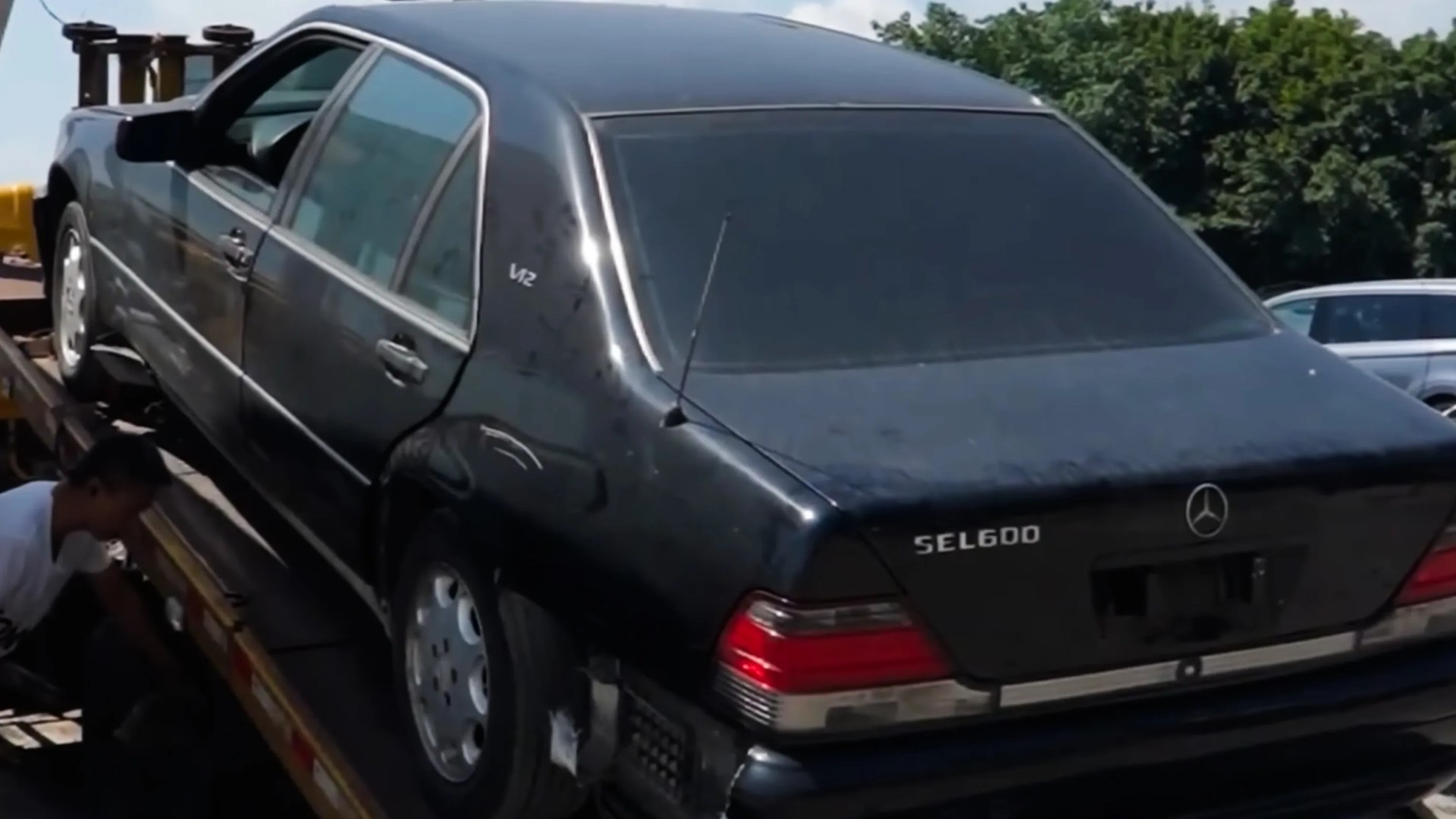 Black Mercedes-Benz SEL600 sedan with V12 badge on flatbed tow truck.
