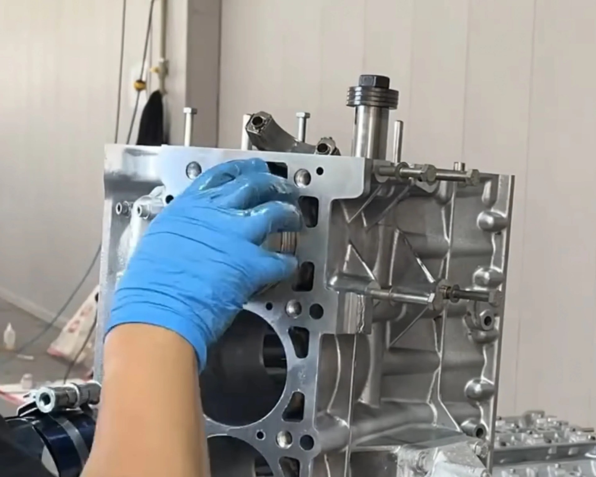 Hand wearing a blue glove assembling or inspecting a silver metal engine block component.