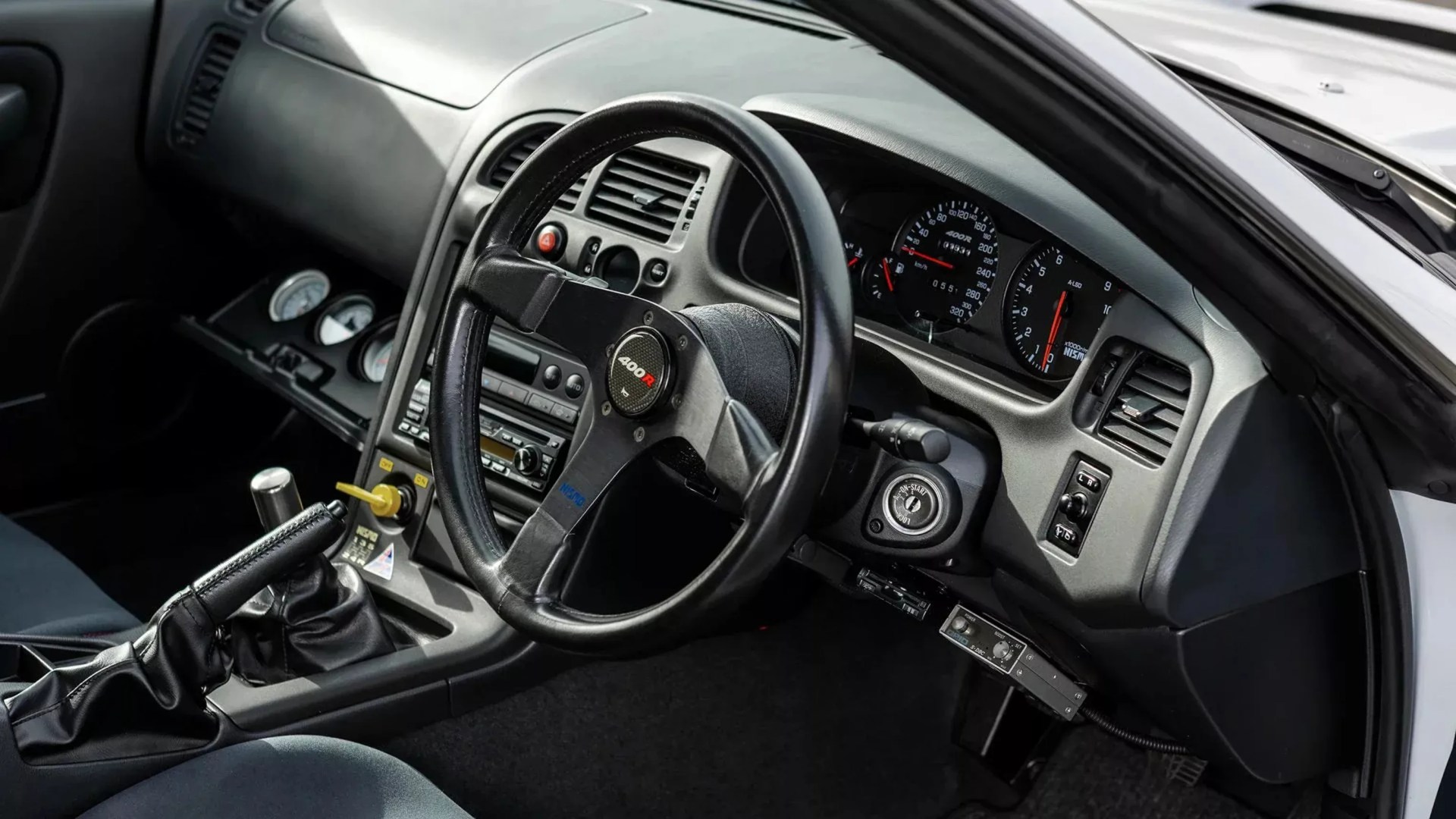Black leather Nismo 400R steering wheel in a right-hand drive car interior with manual gear shift and additional gauges.