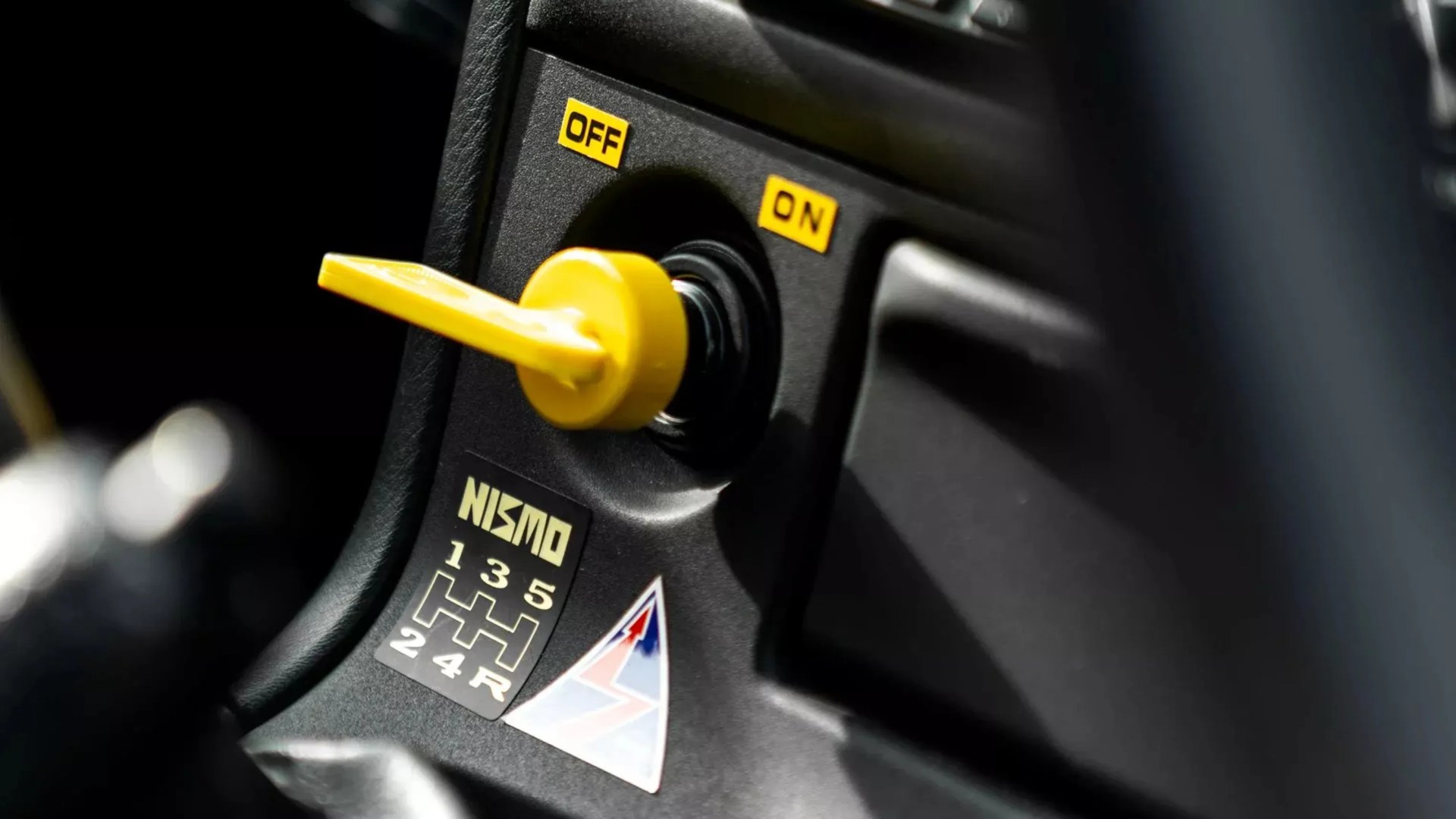 Yellow toggle switch set to ON on a black panel with NISMO gear pattern decal.
