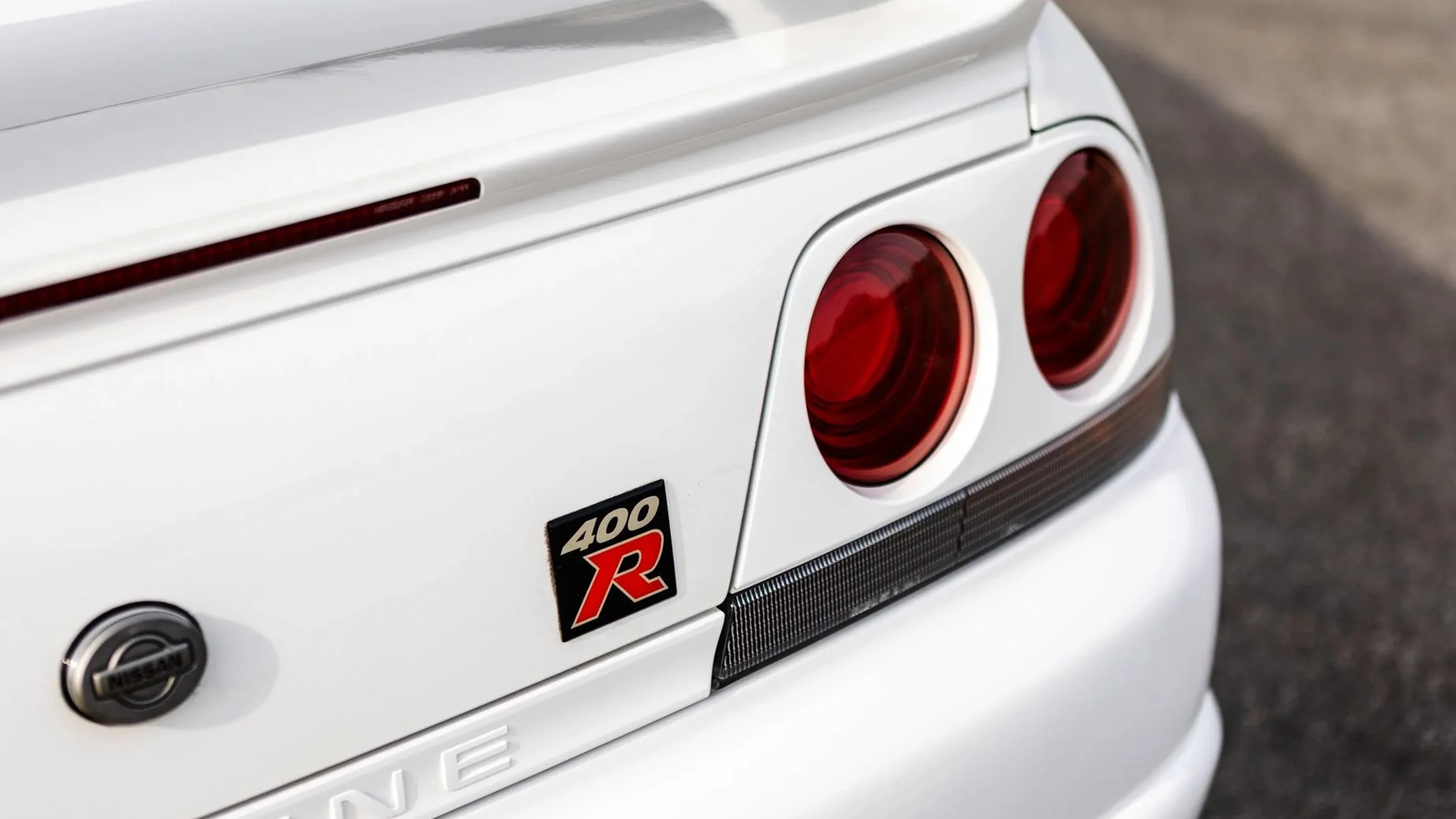 Close-up of white Nissan Skyline 400R rear with round red taillights and emblem badge.