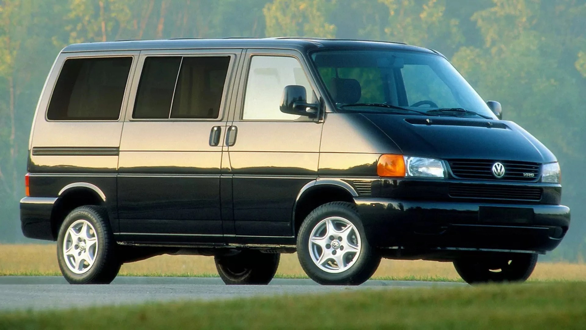 Black and silver Volkswagen van with sliding side doors parked on a road with trees in the background.