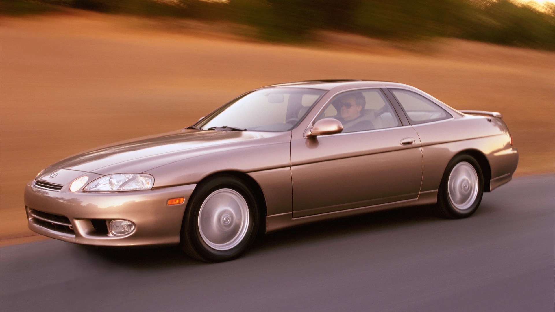 Bronze two-door coupe car driving on a road with blurred background.