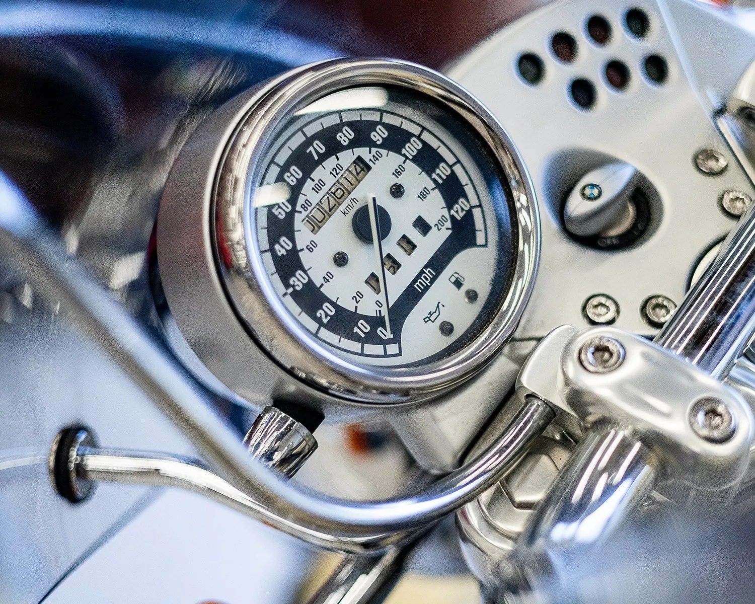 Close-up of a motorcycle speedometer with chrome casing and handlebars.