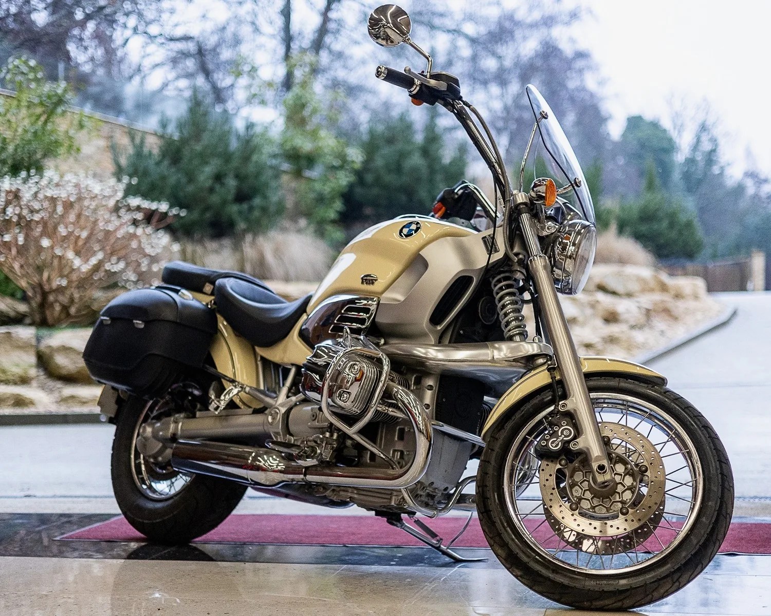 Cream and chrome BMW motorcycle with black leather seat and saddlebags parked on a polished floor.