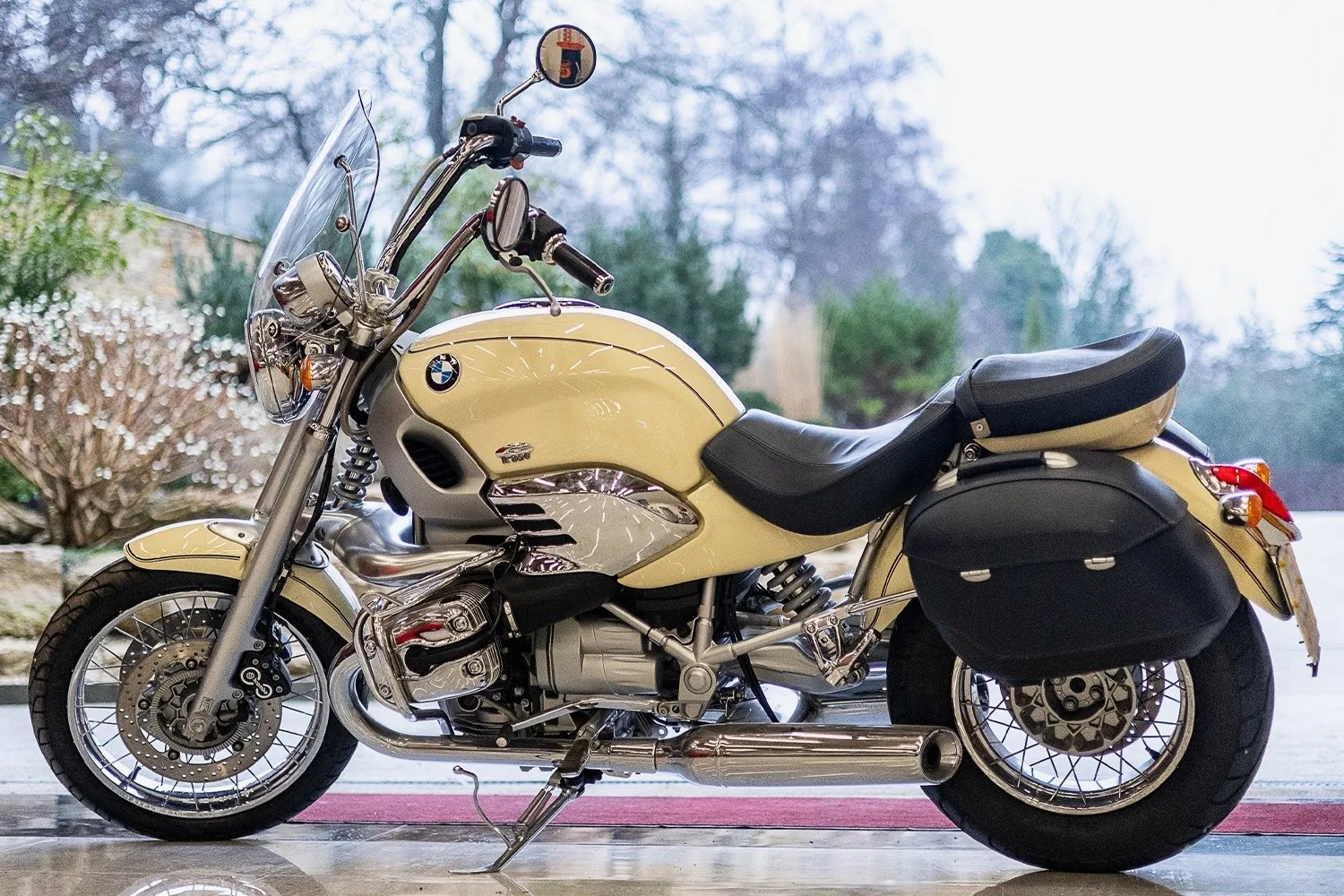 Cream BMW R1200 motorcycle with black leather seat and saddlebags parked indoors.