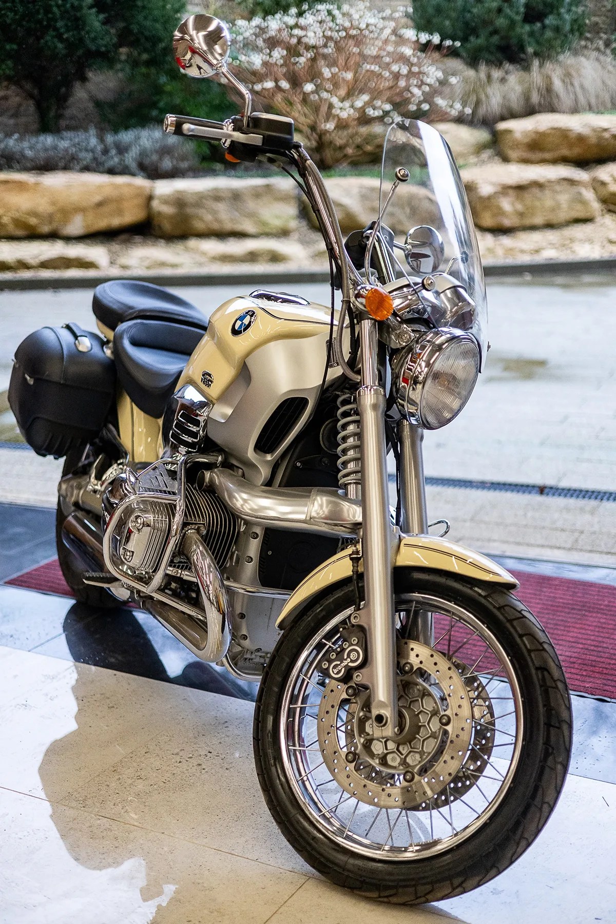Cream-colored BMW motorcycle with black leather seats, chrome details, and a clear windshield parked indoors.