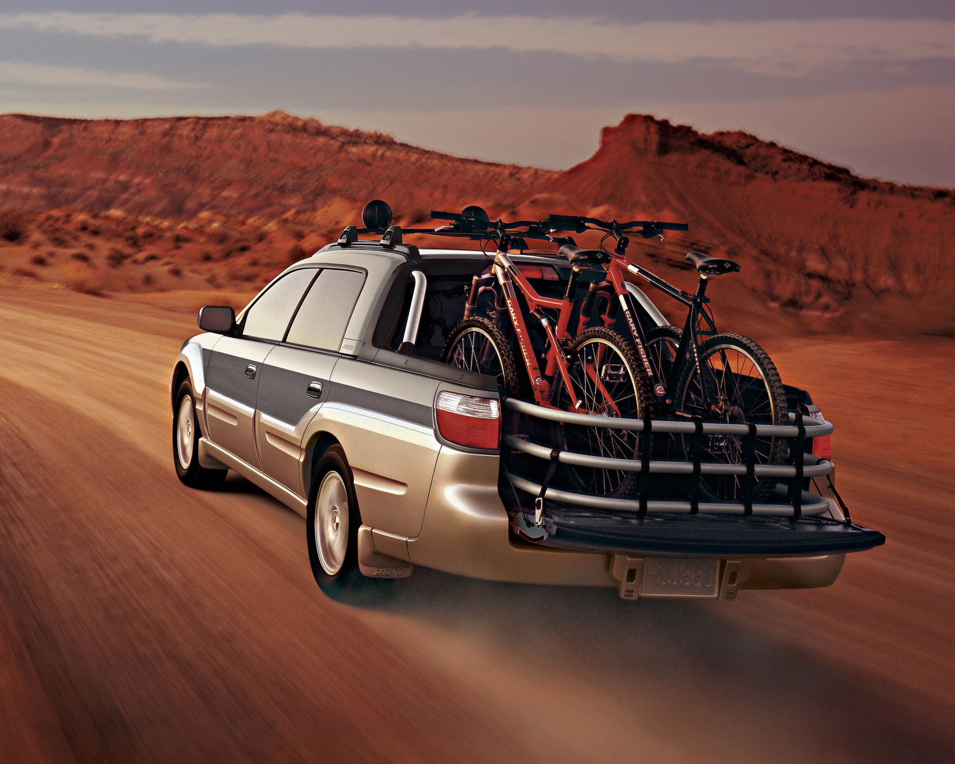 Silver and gray pickup truck driving on a dirt road with two mountain bikes secured in the open bed.
