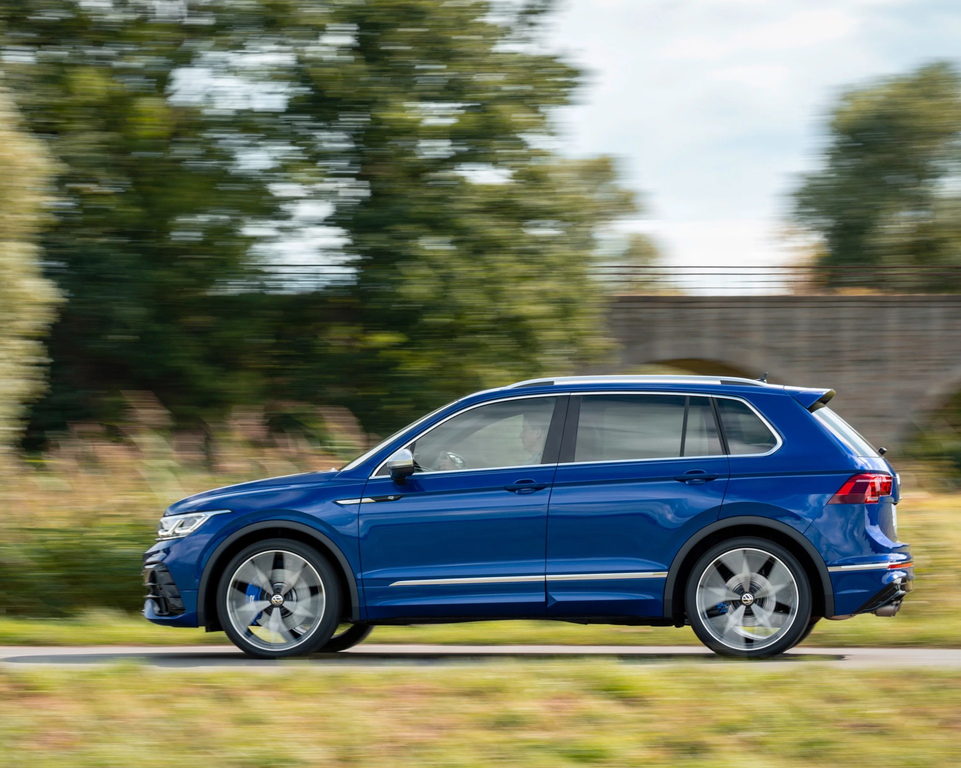 Blue Volkswagen Tiguan SUV driving on a road with blurred green trees in the background.