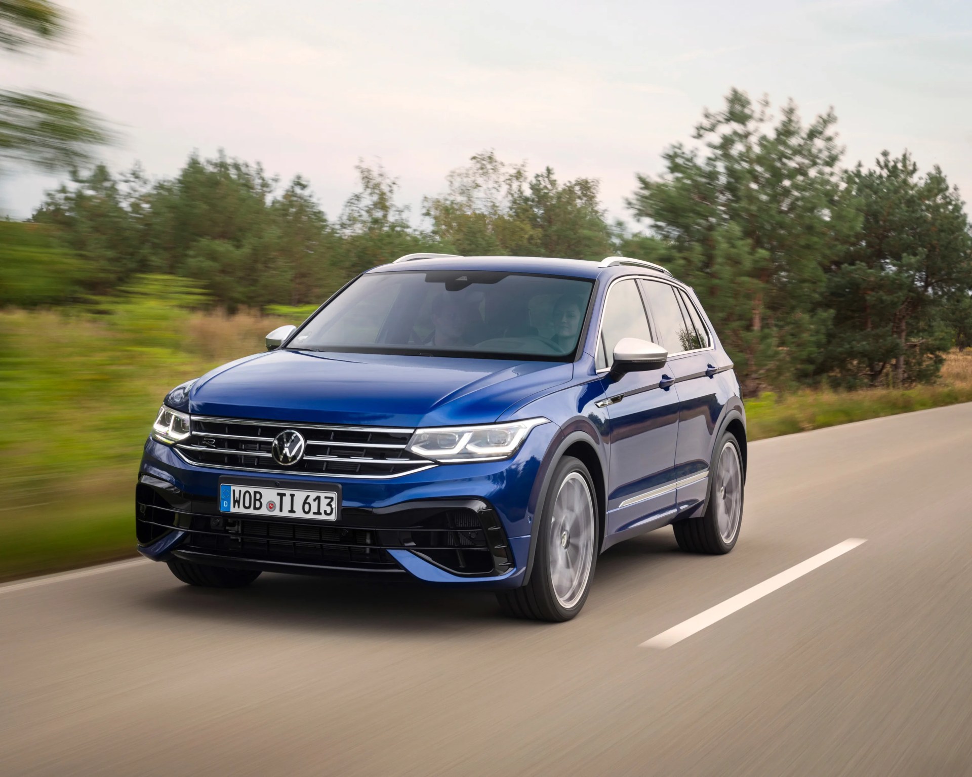 Blue Volkswagen Tiguan R SUV driving on a road with blurred trees in the background.