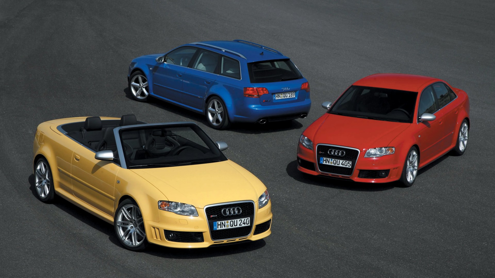 Three Audi RS4 cars in yellow convertible, blue wagon, and red sedan parked on asphalt.
