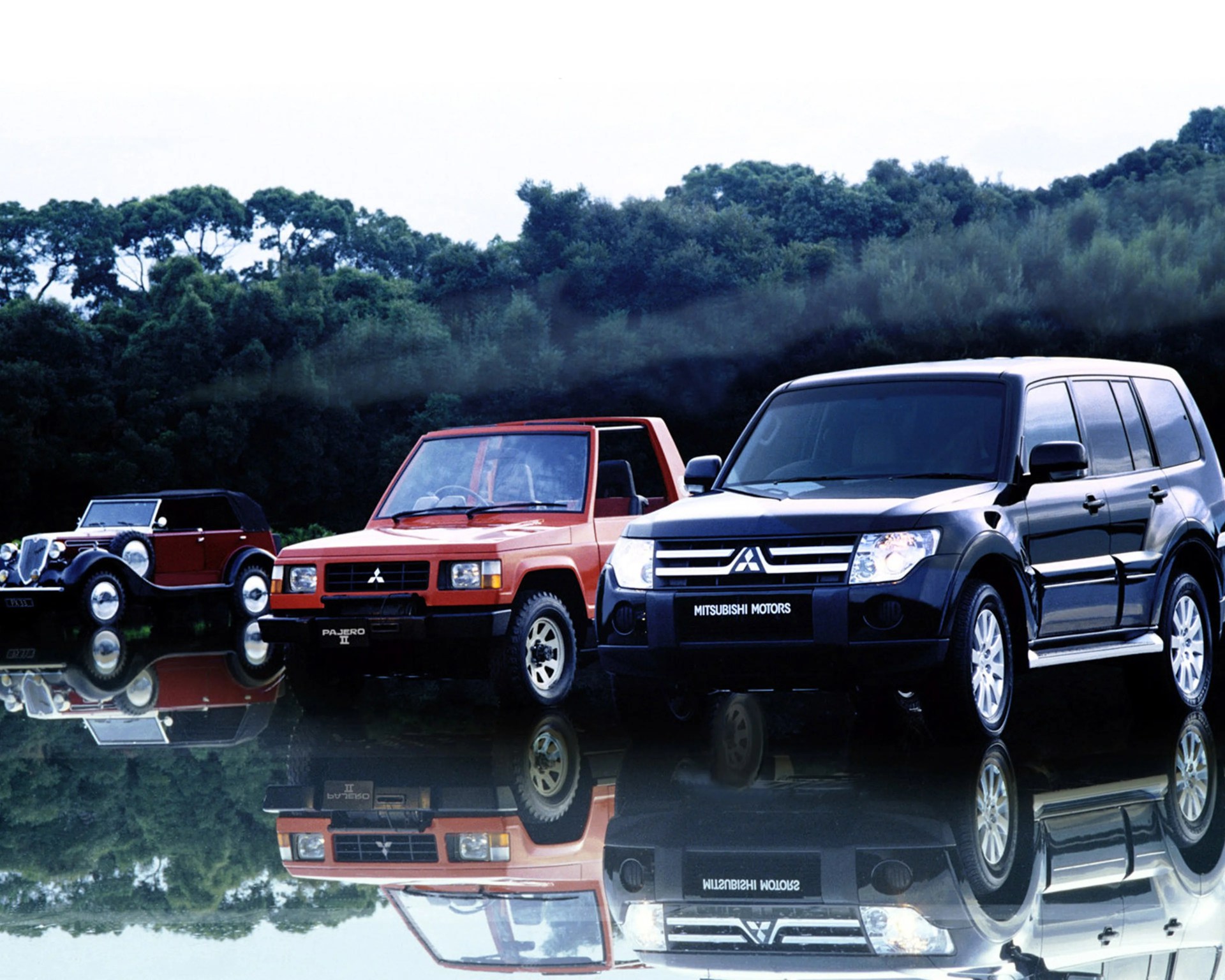 Three Mitsubishi SUVs in different eras, black modern, red mid-generation, and vintage maroon, reflected on a glossy surface with trees in the background.